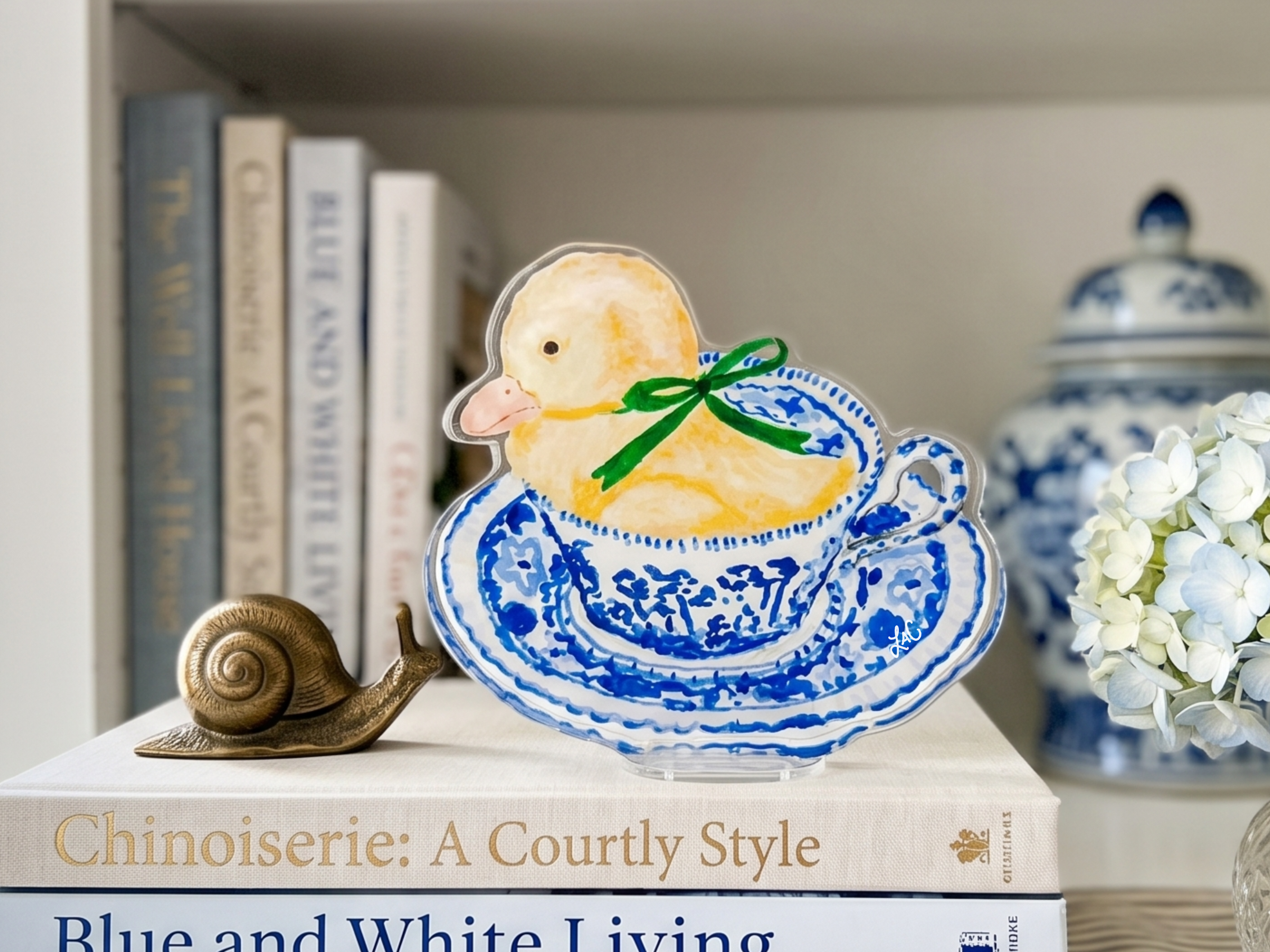 a decorative ceramic duck sitting on top of a stack of books, with a small brass snail figurine placed next to it.