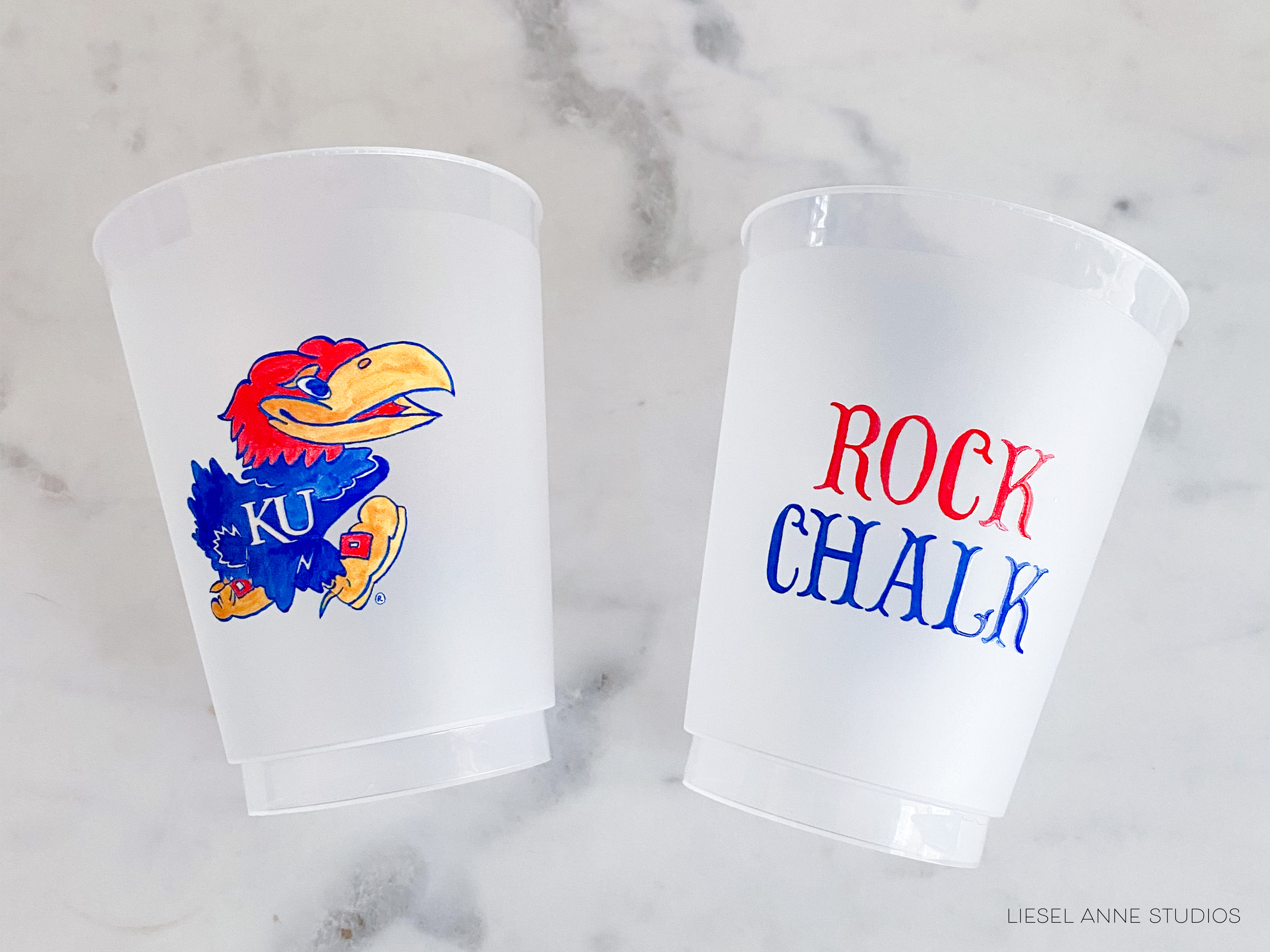 Two white plastic cups with colorful designs on them, one featuring a bird and the other with the words "Rock Chalk" written on it.