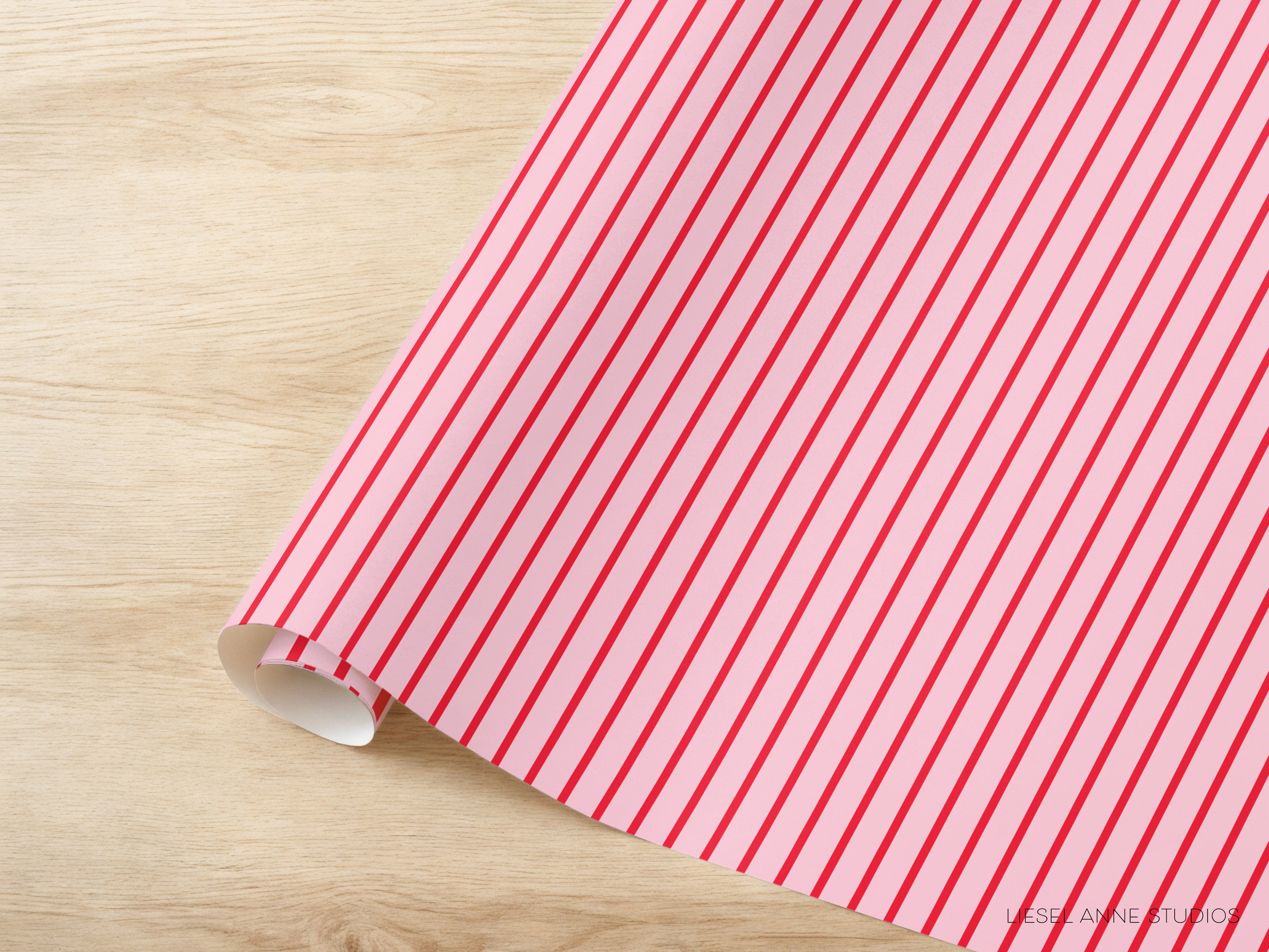 A roll of pink and red striped wrapping paper is placed on a wooden surface.