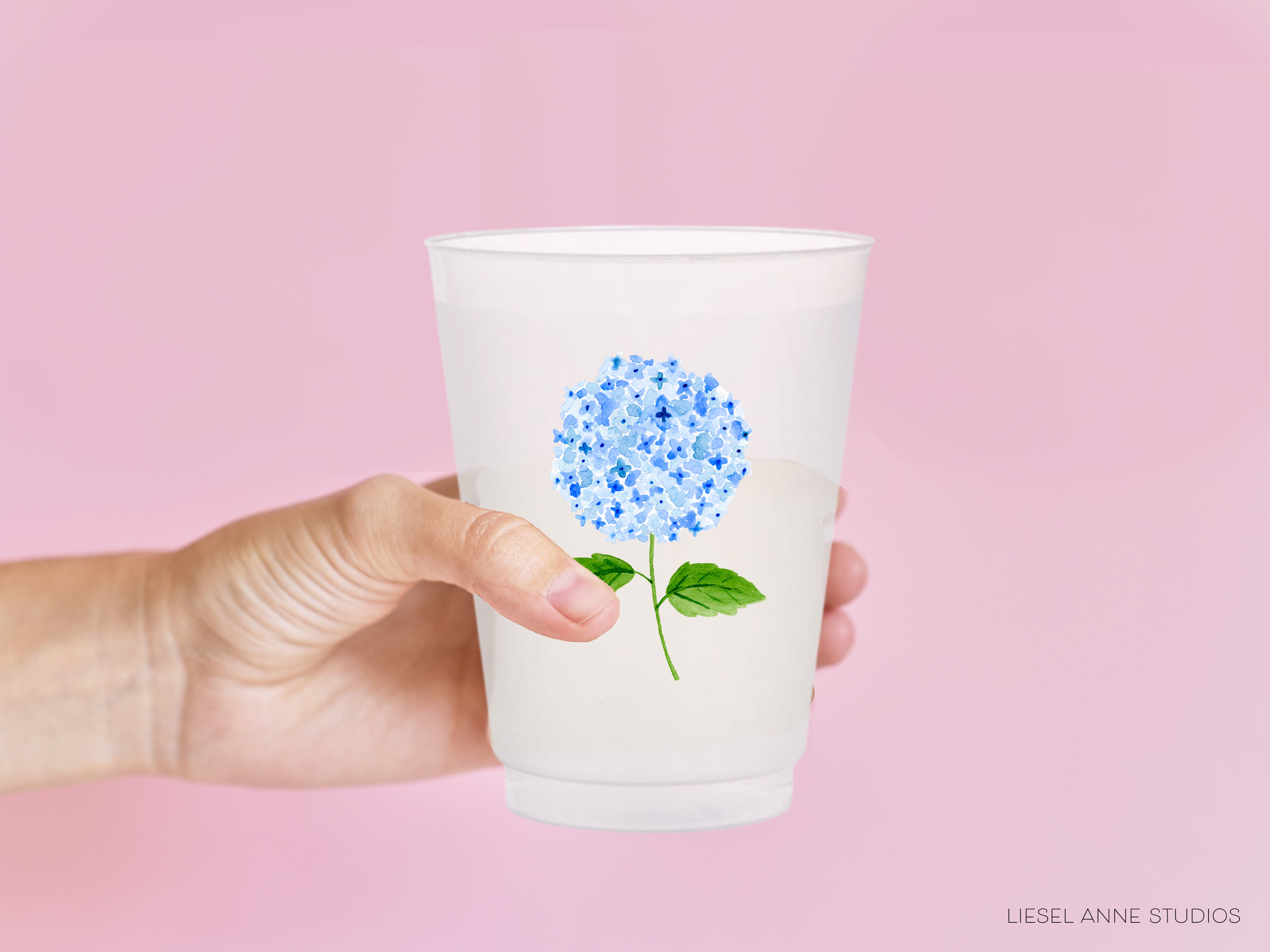 a hand holding a glass with a blue flower painted on it