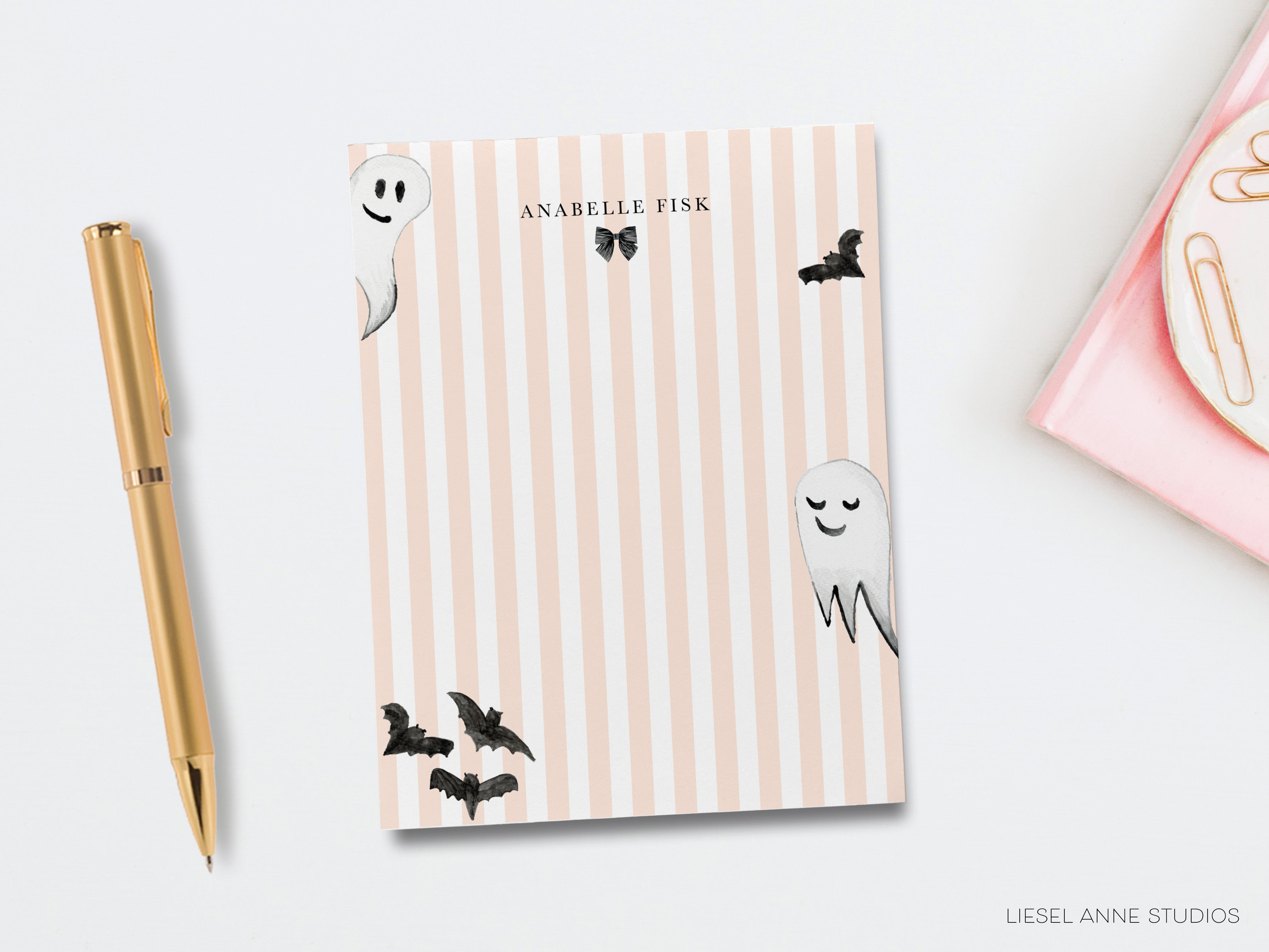 a pink and white striped notebook with a gold pen and a gold stapler on a white background.