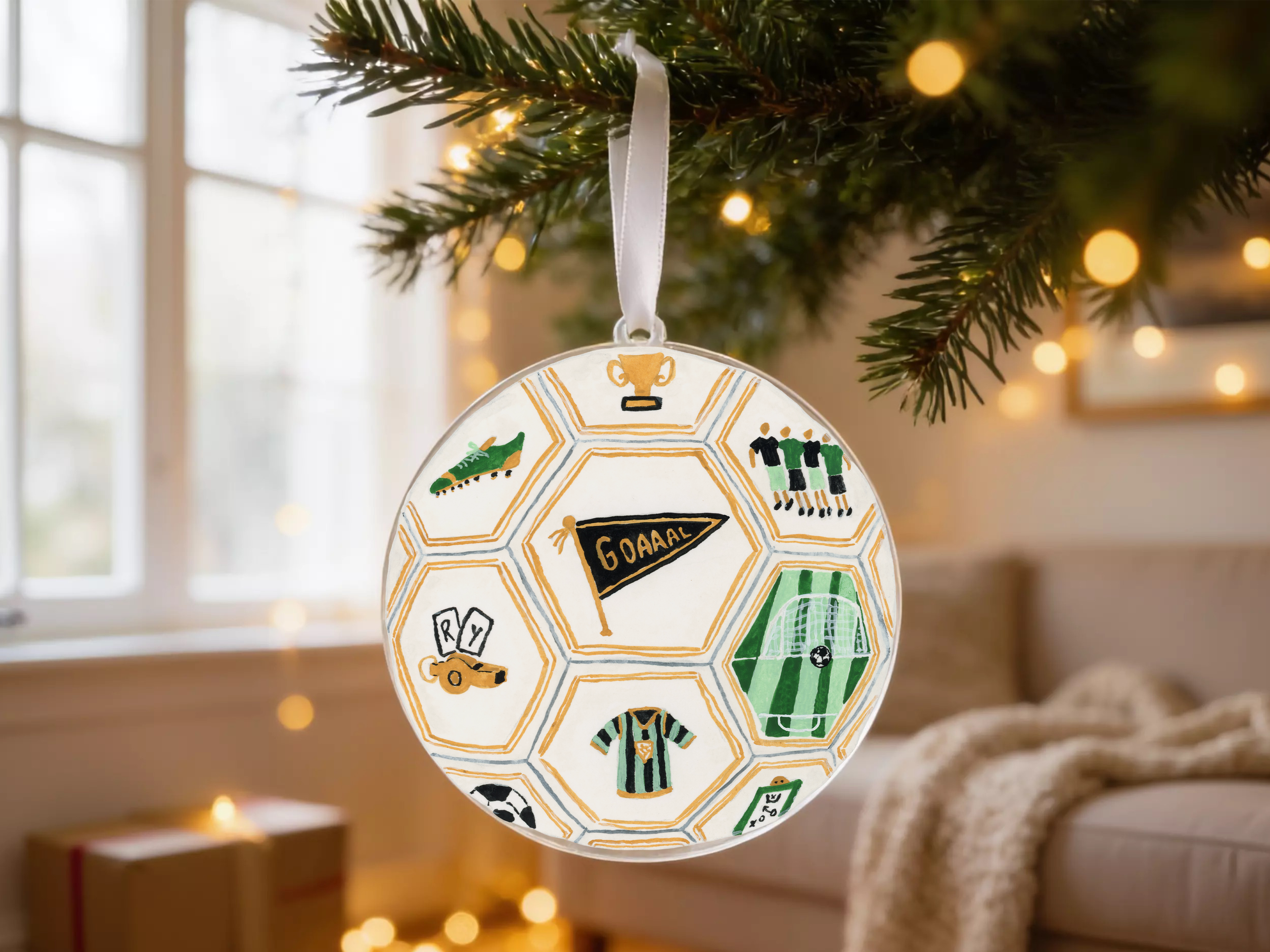 A round ornament hanging from a Christmas tree, featuring various soccer-related icons and designs.