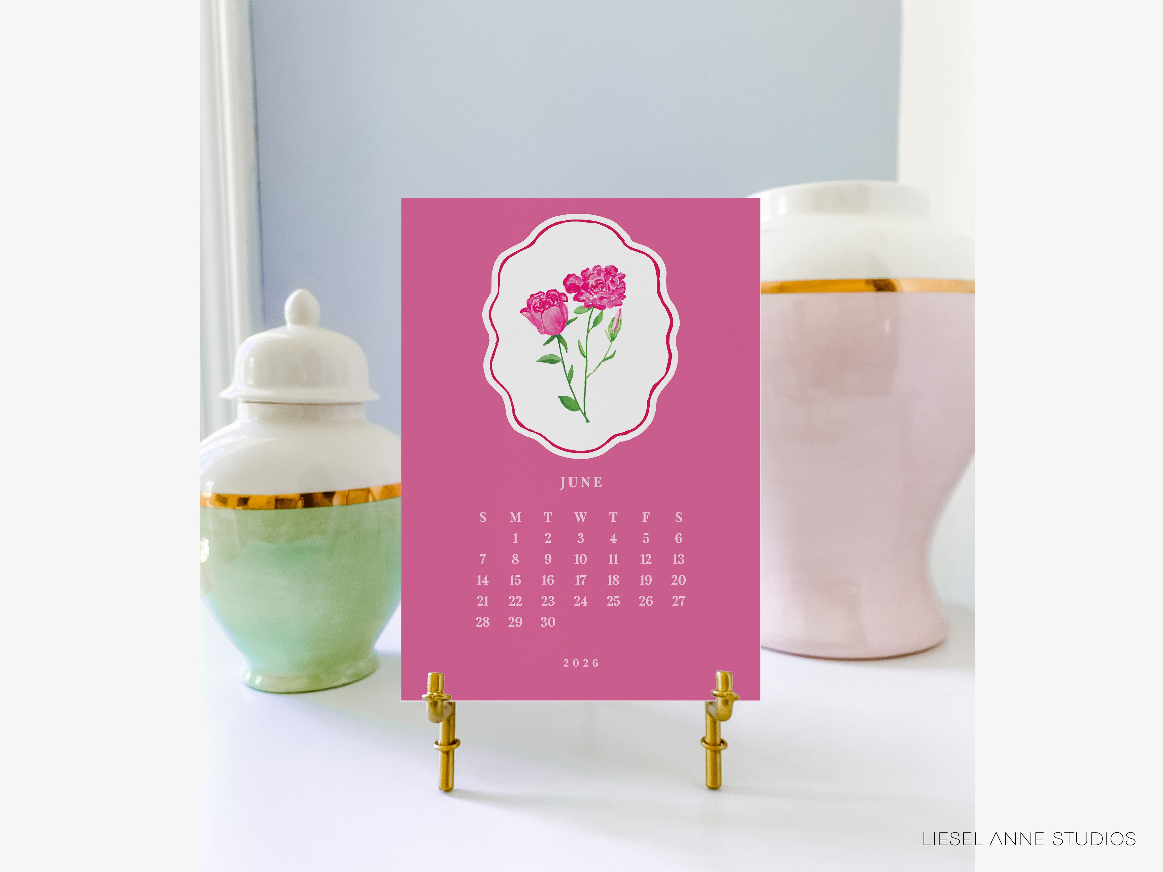 a pink calendar with a floral design, placed on a stand between two decorative vases.