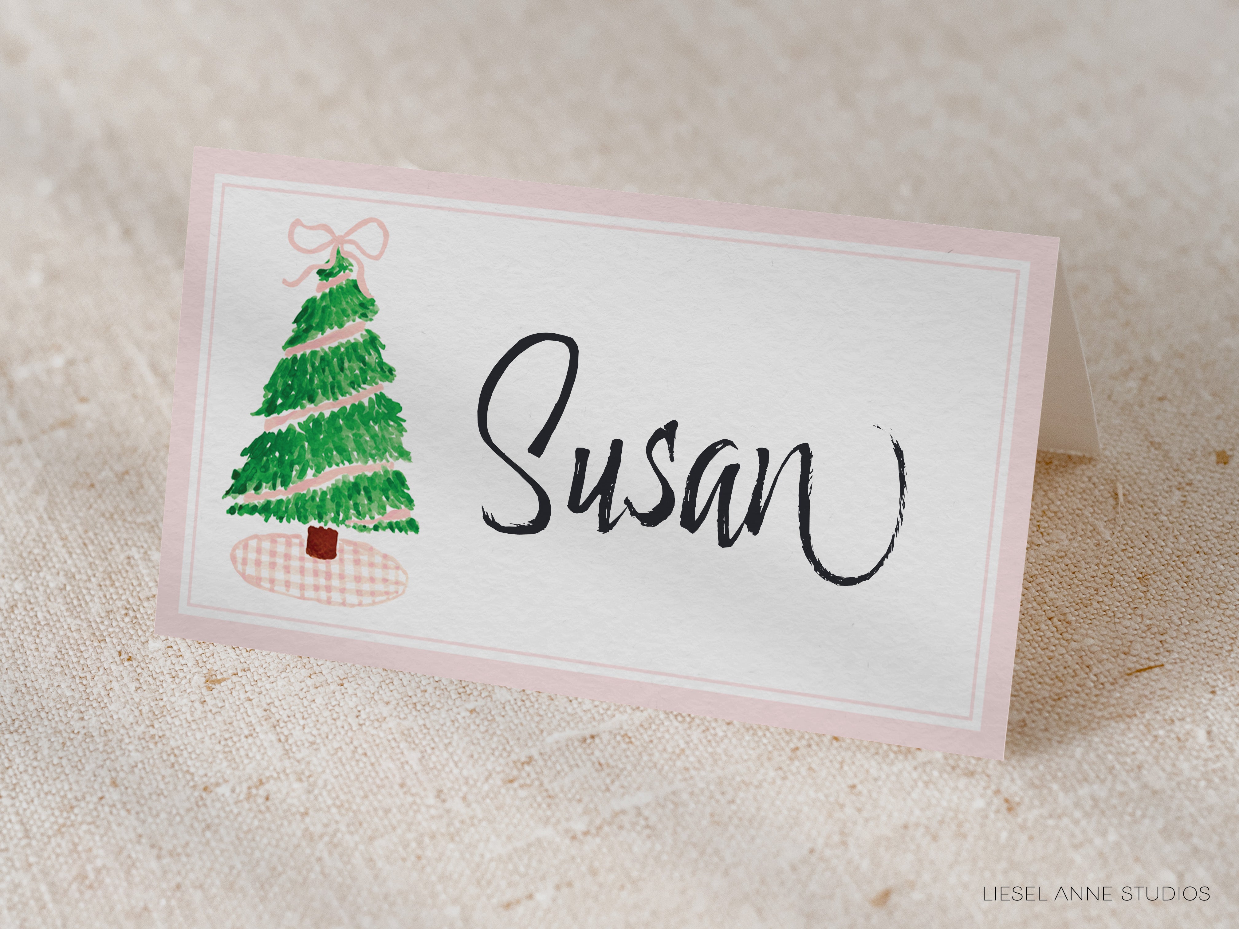 A pink name card with a Christmas tree illustration and the name "Susan" written on it.
