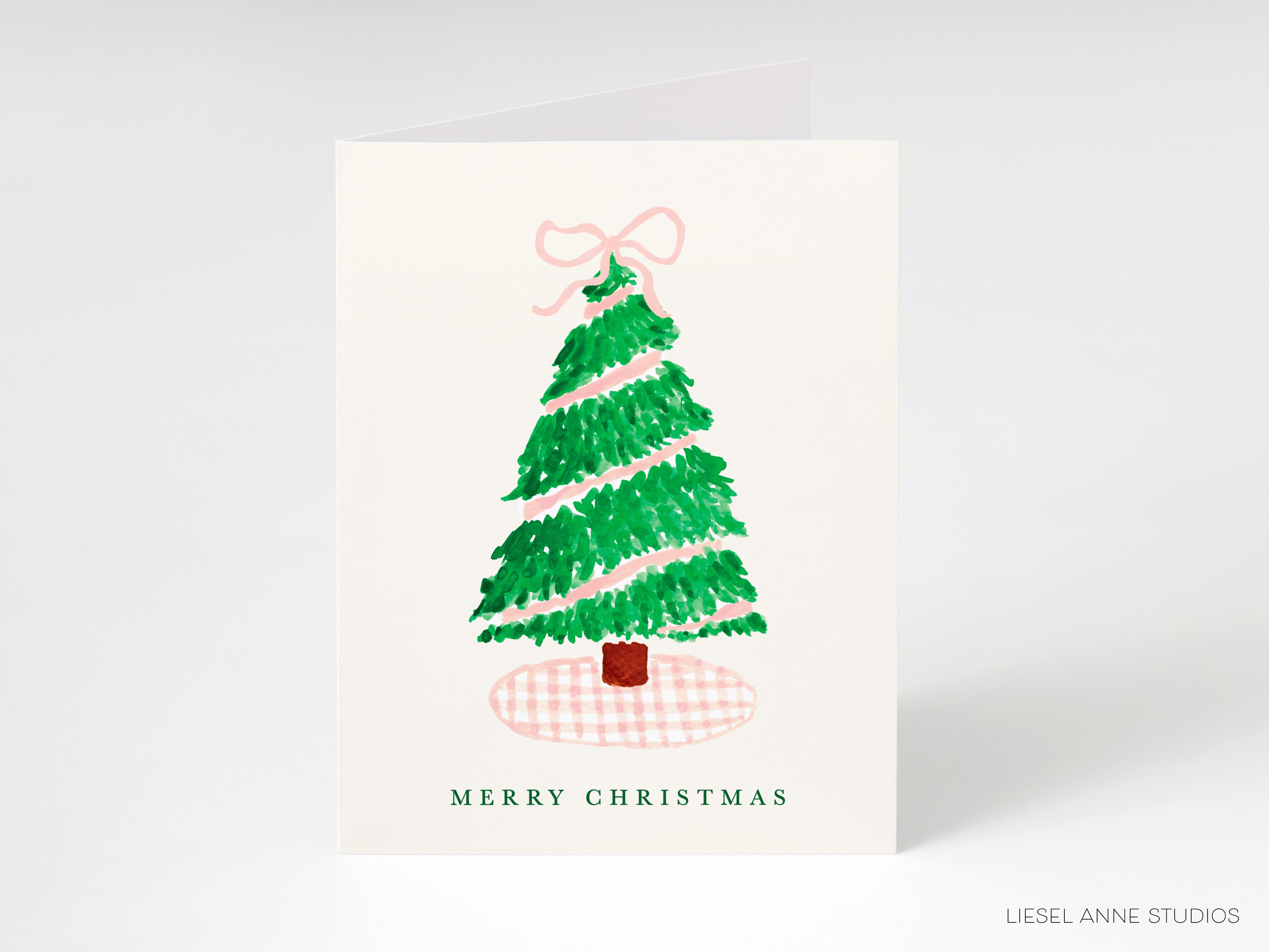 A Christmas card with a green tree and a pink bow on top, along with the text "MERRY CHRISTMAS" printed on it.