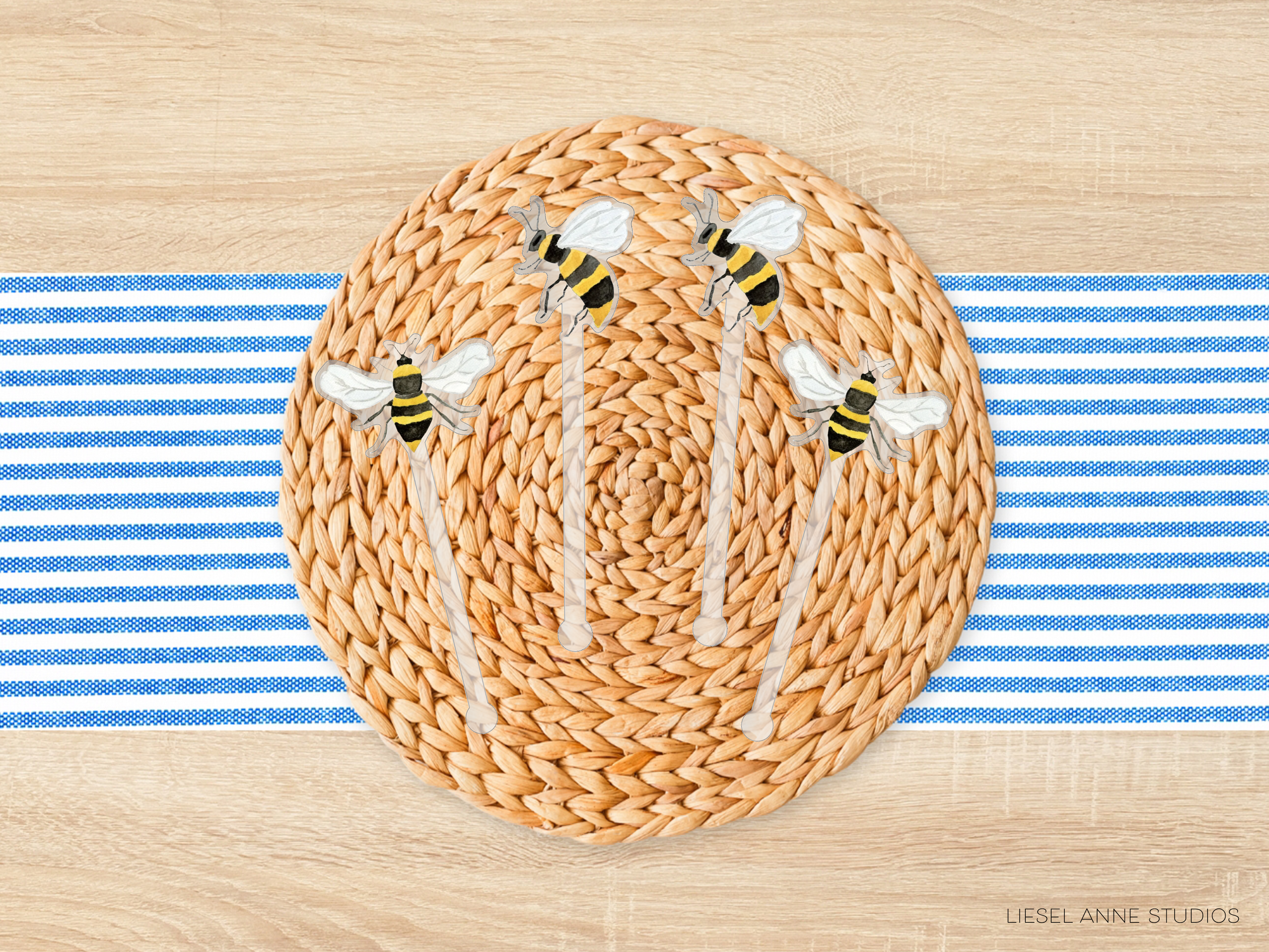 A woven placemat with a circular design featuring four bee-like figures, placed on a wooden surface with blue and white striped fabric.