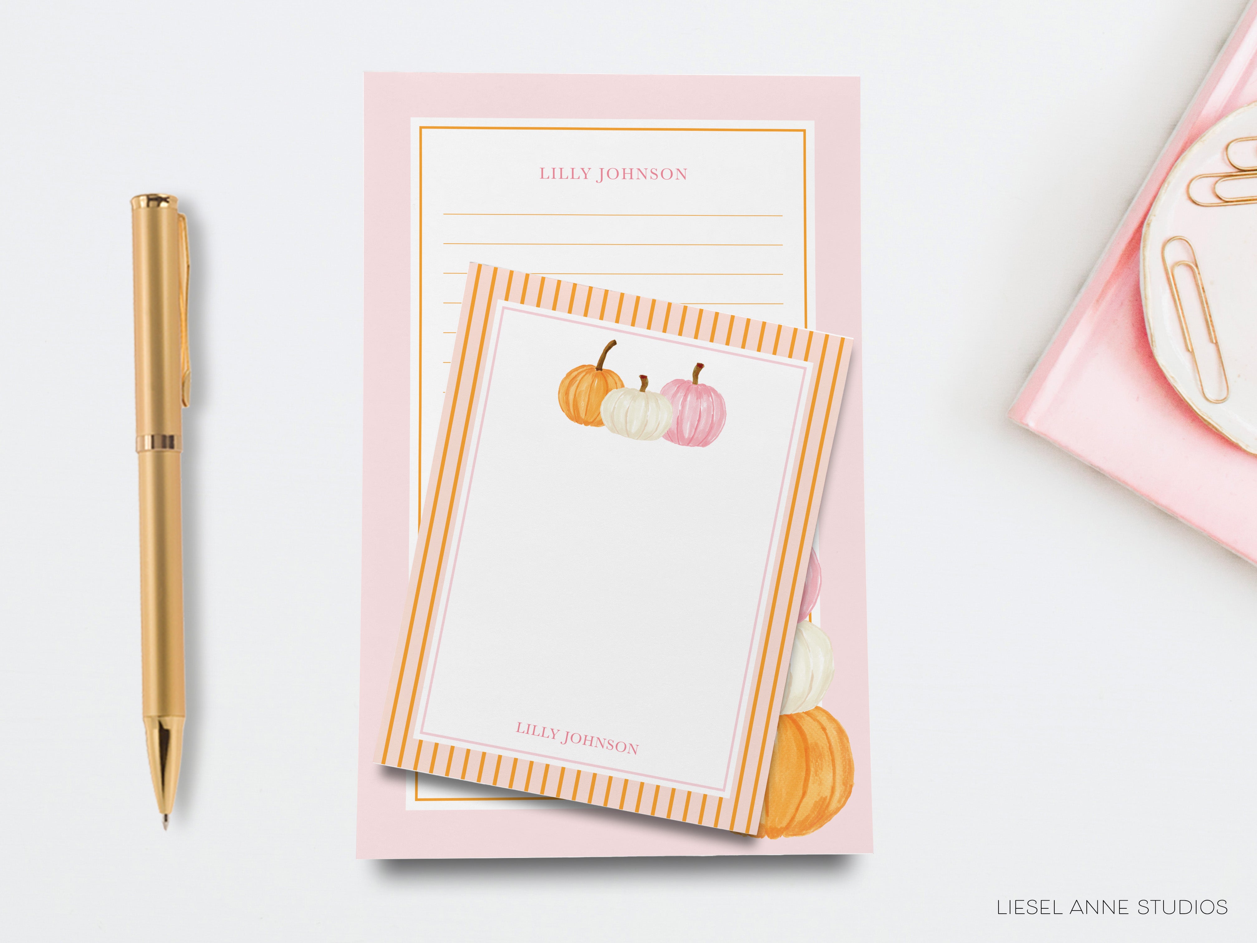 a pink notepad with a gold pen and a gold stapler on a white background.