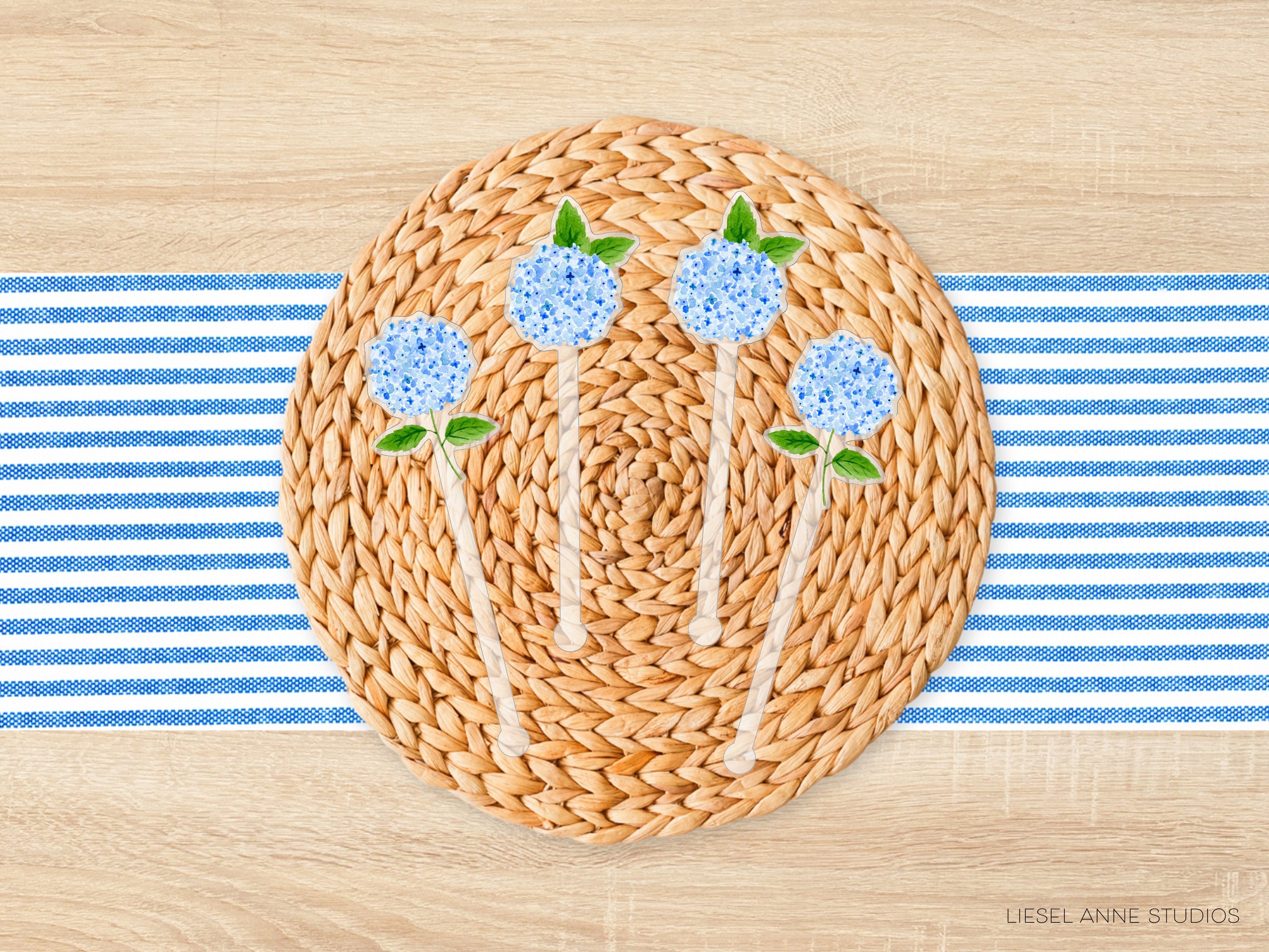 A woven placemat with blue flowers and green leaves, placed on a wooden table with blue and white striped napkins.