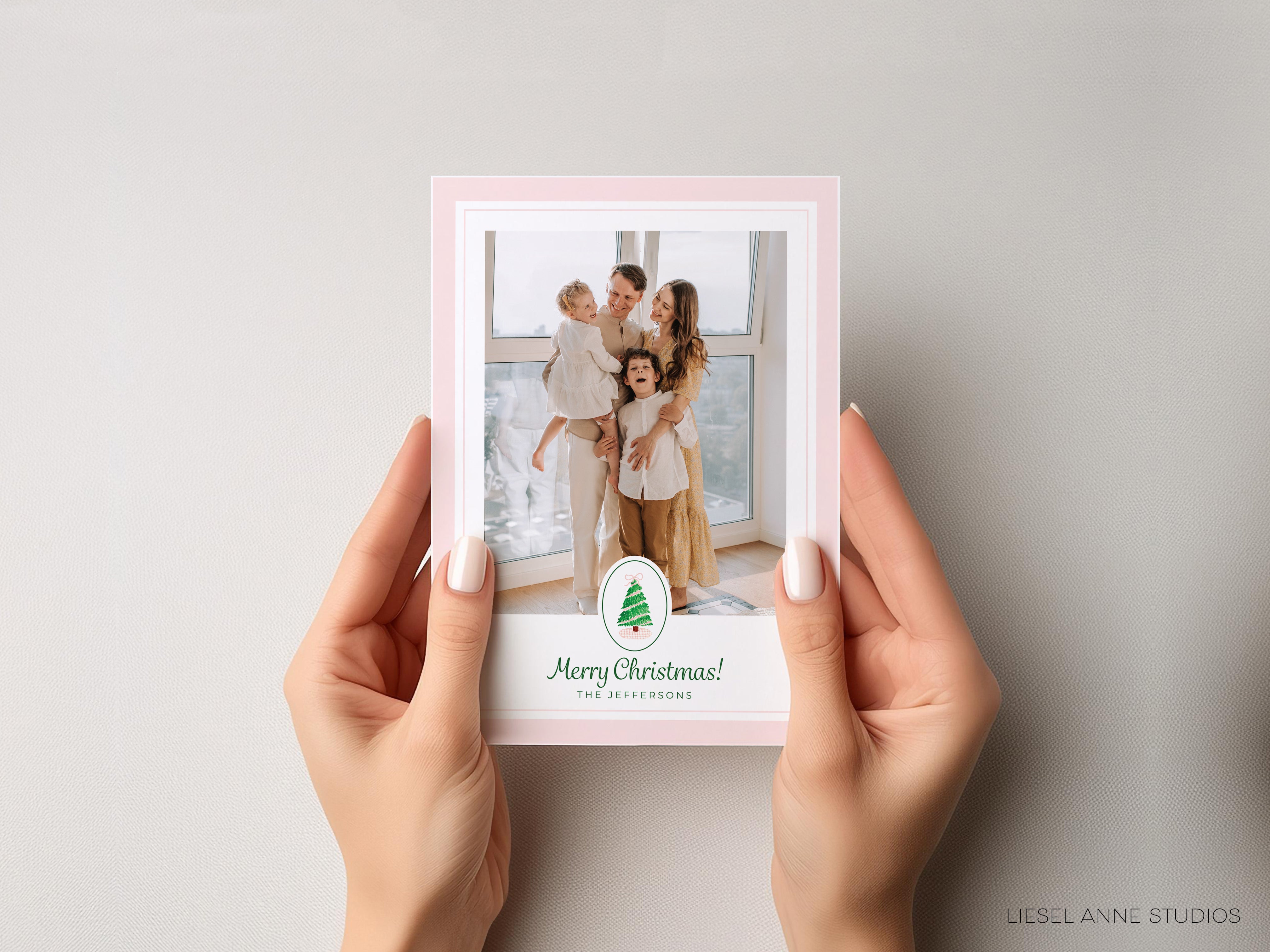 A pair of hands holding a pink-framed photo of a family, with a Christmas-themed greeting on the bottom of the frame.