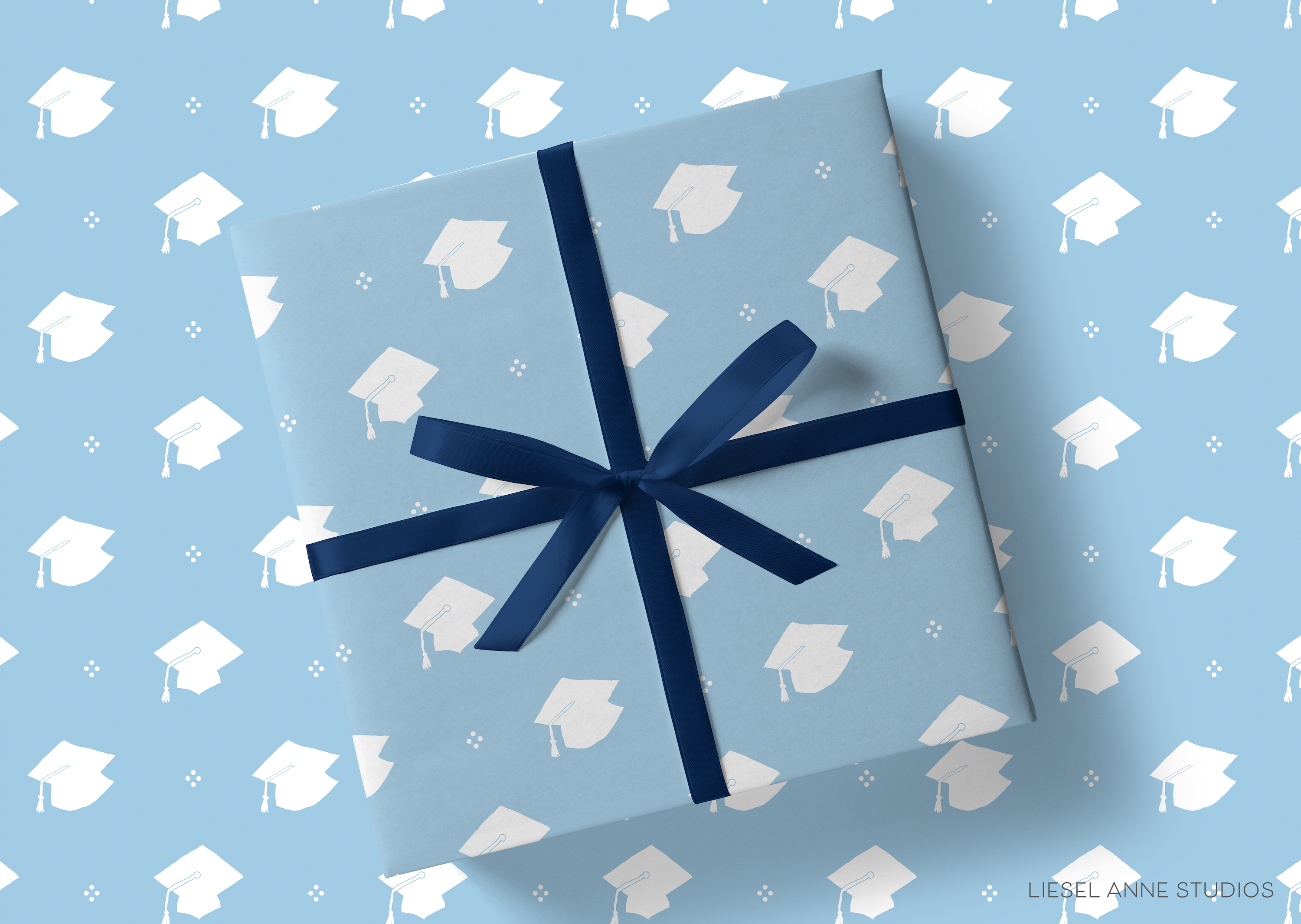 A gift wrapped in blue paper with a white graduation cap pattern, tied with a blue ribbon.