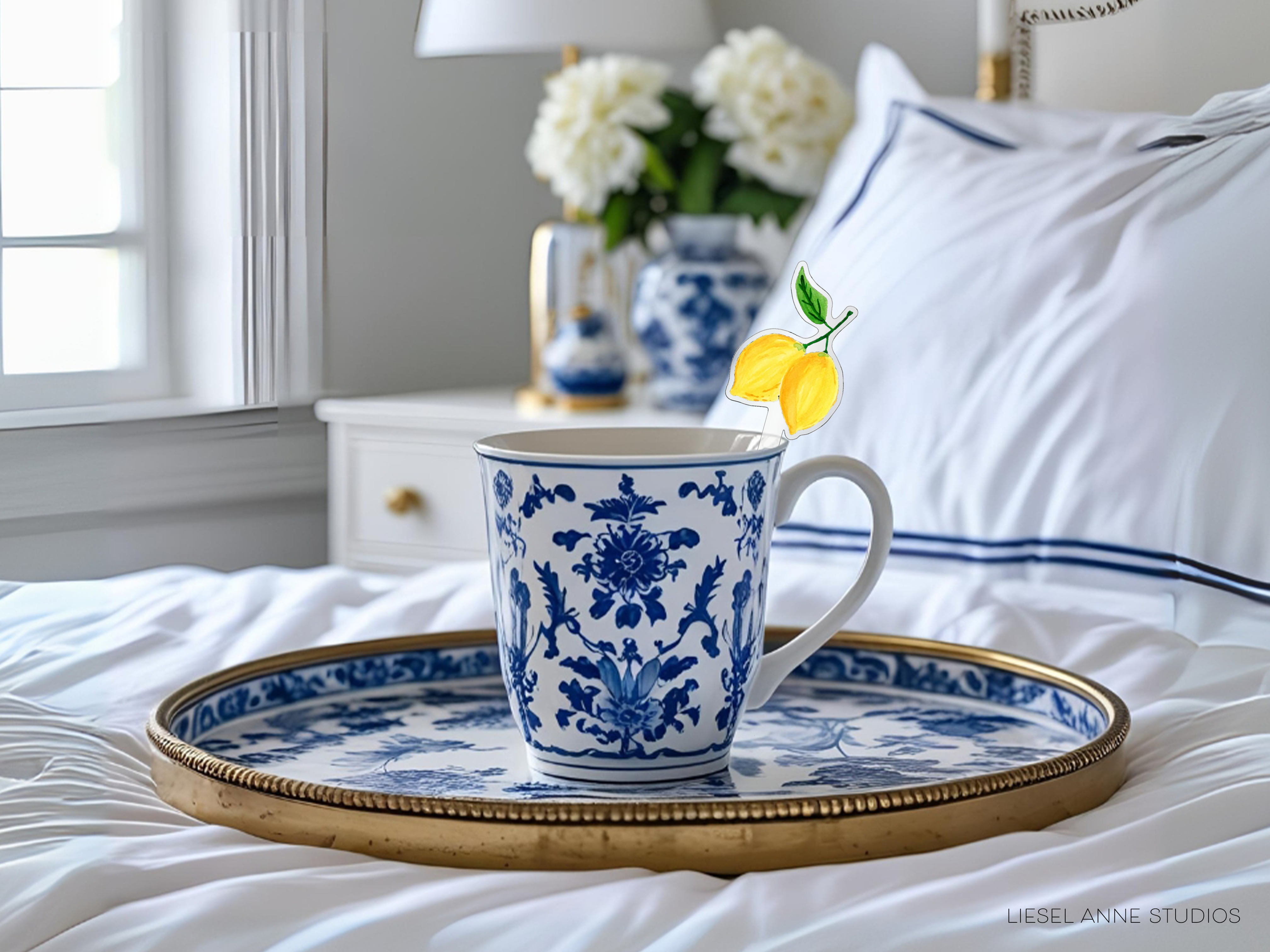 A blue and white patterned coffee mug sits on a gold tray, with a vase of white flowers and a yellow lemon decoration in the background.