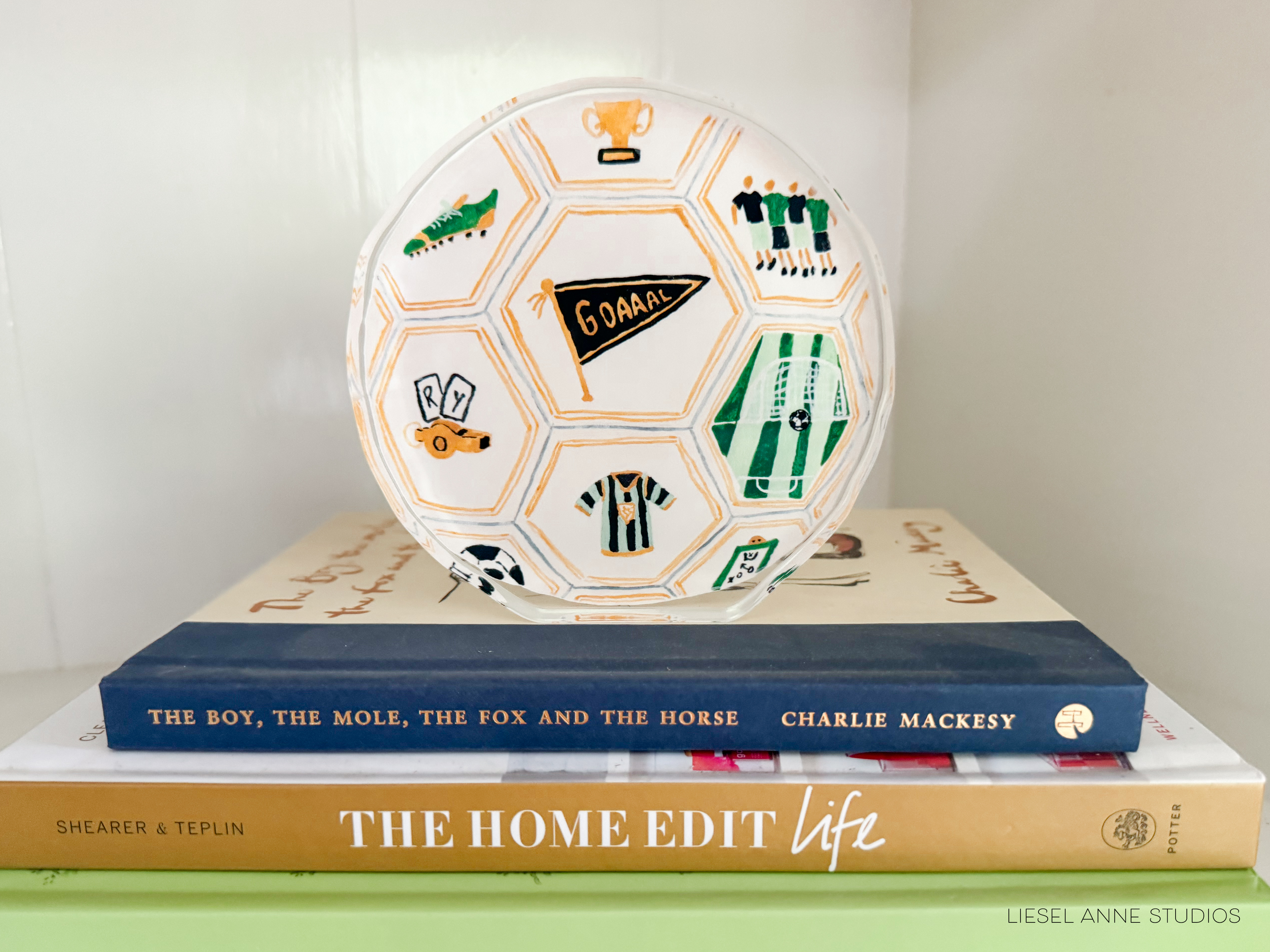 a soccer ball with various sports-themed illustrations, such as a trophy, a soccer ball, and a flag, placed on top of a stack of books.