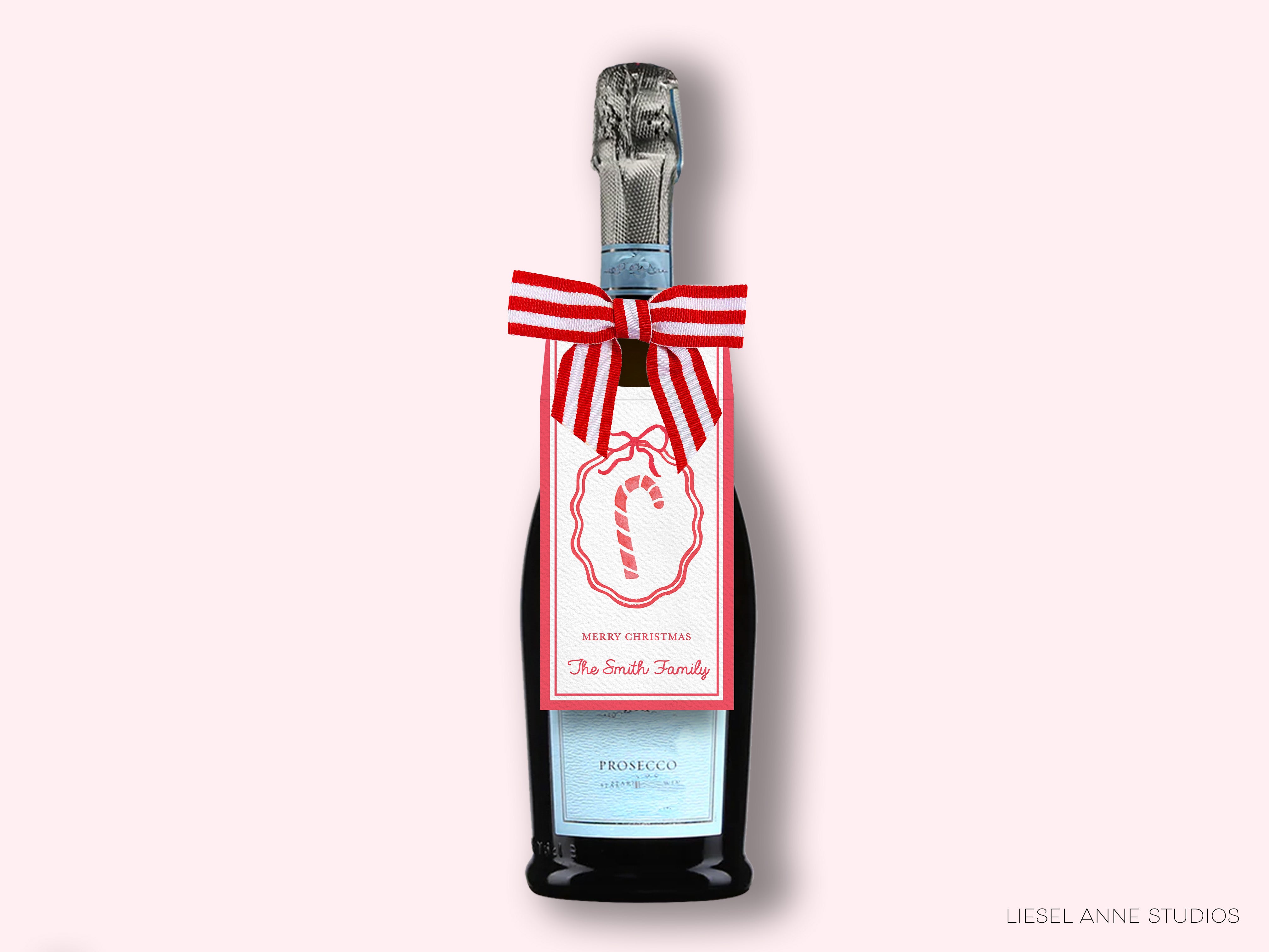 A bottle of Prosecco with a festive red and white striped ribbon and a candy cane design on the label, set against a pink background.