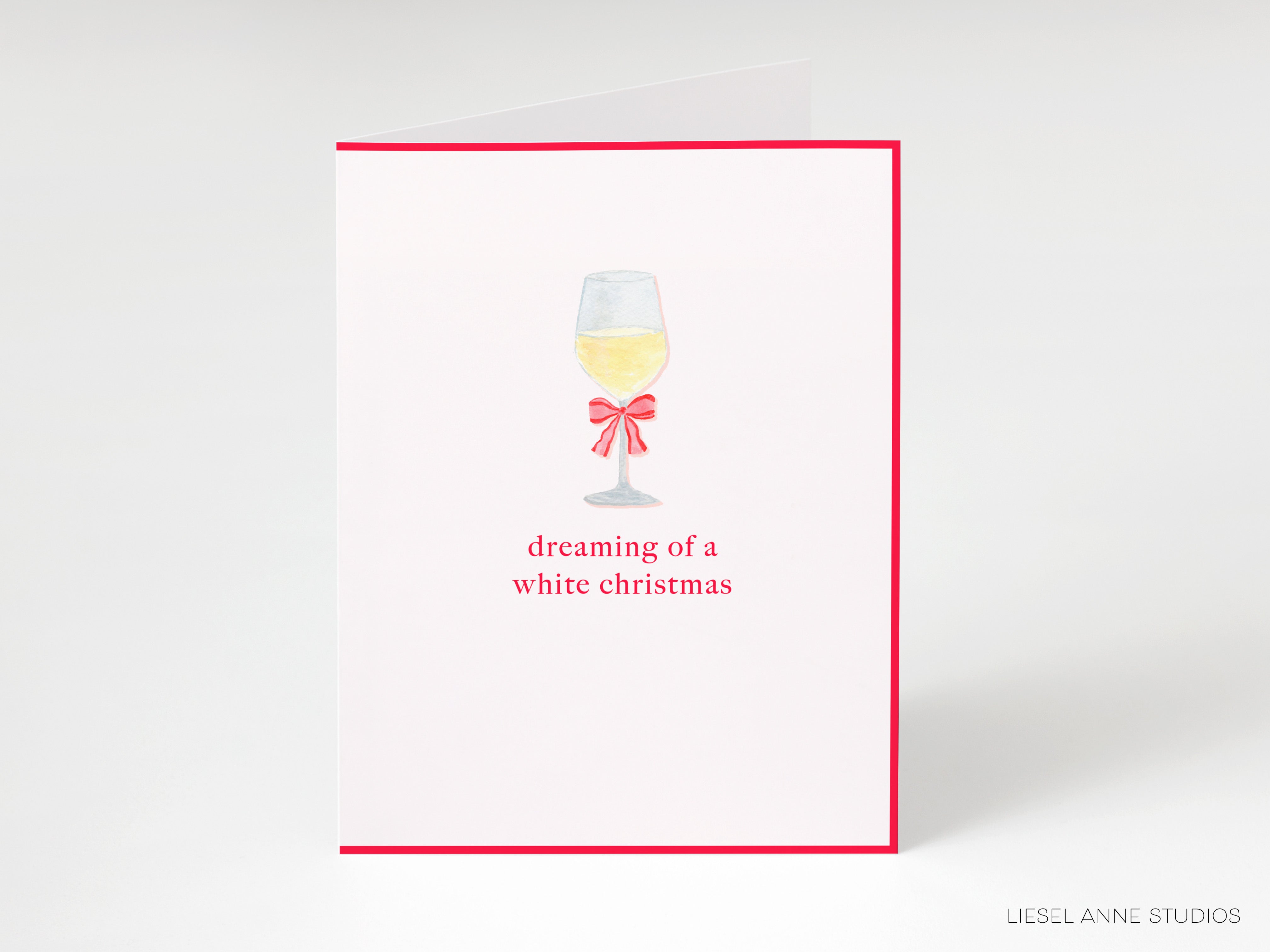 A white card with a red border, featuring an illustration of a wine glass with a bow and the text "dreaming of a white christmas".