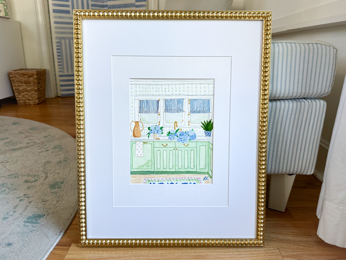 a framed illustration of a kitchen scene with a sink, cabinets, and various kitchen accessories.