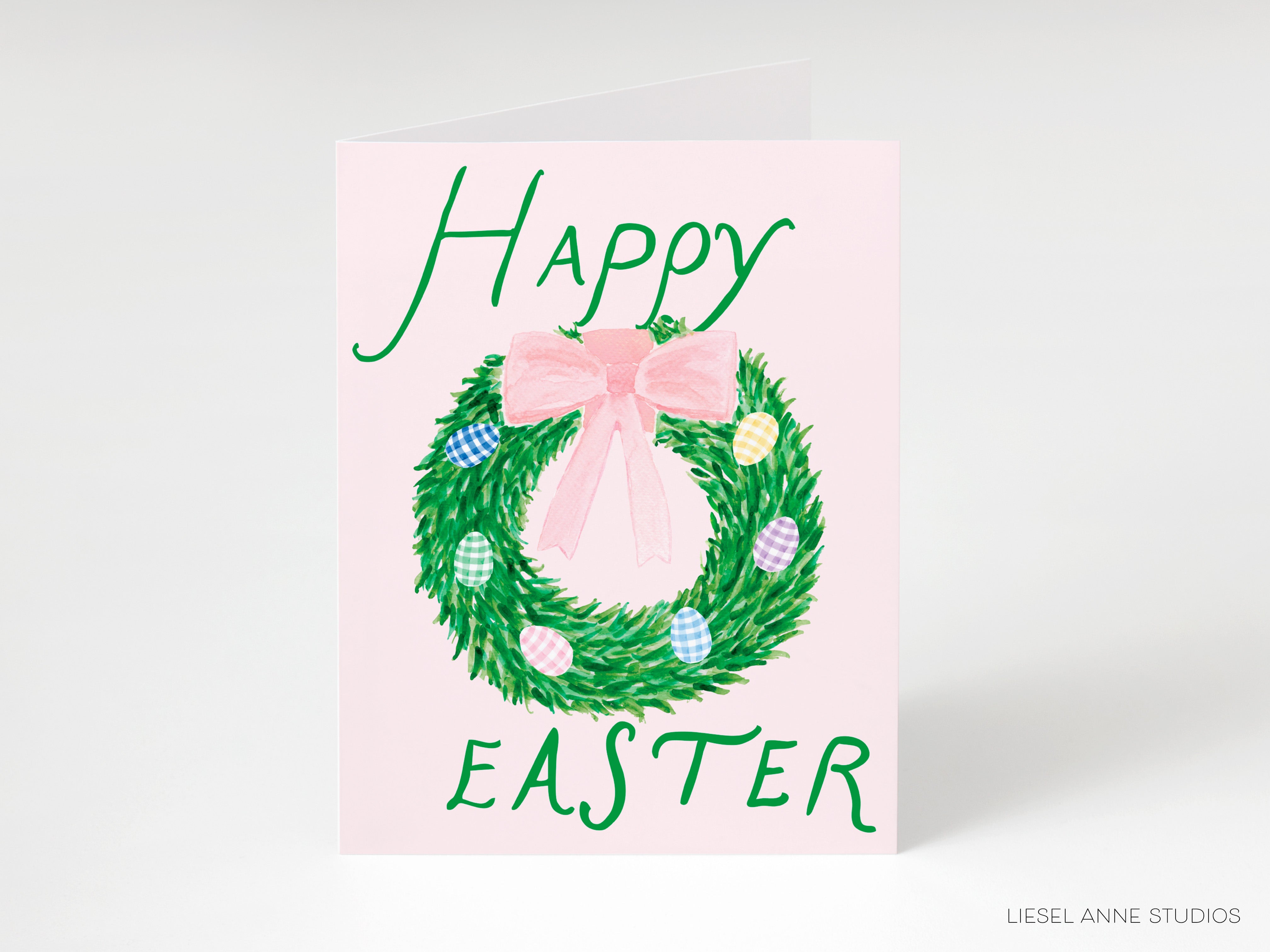 A pink Easter greeting card with a wreath of green leaves and colorful Easter eggs.