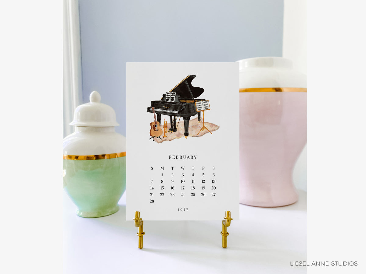 February music page of the Happy Hobbies 2027 desk calendar on a gold easel, a gift for music lovers