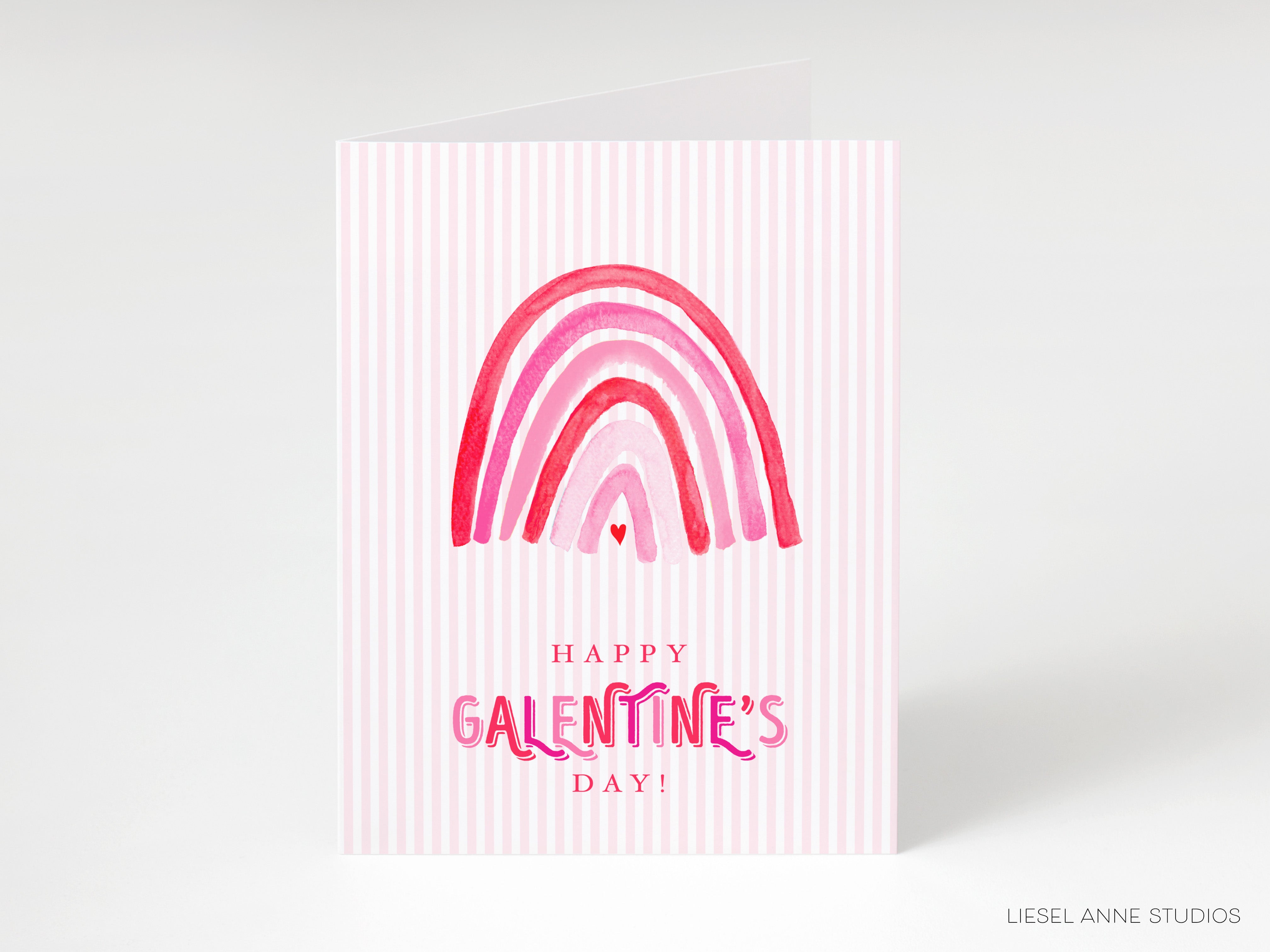 A pink and white striped greeting card with a rainbow graphic and the text "Happy Galentine's Day!"