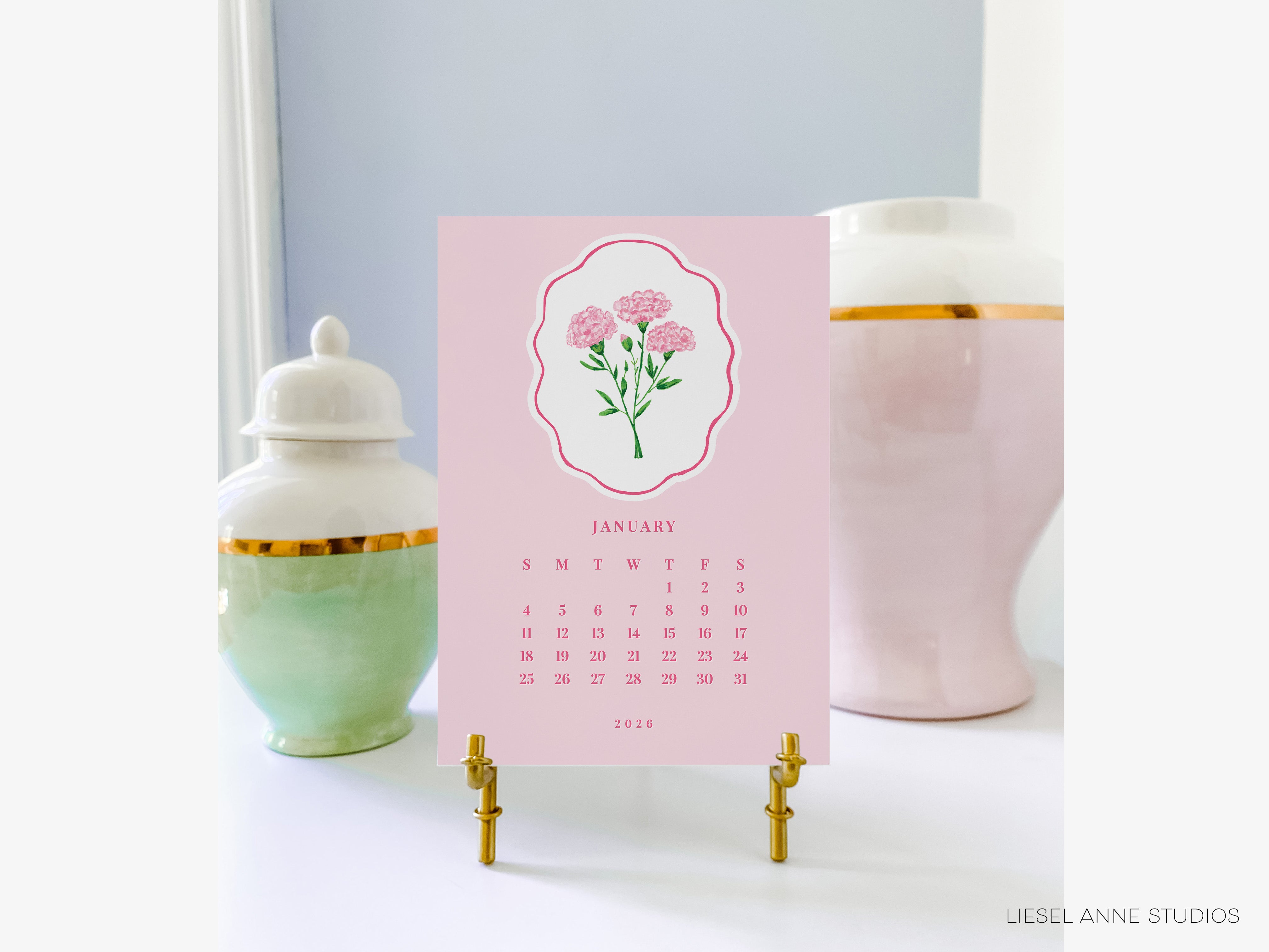 A pink and white calendar displaying the month of January, with a floral illustration, is placed on a white surface between two decorative vases.