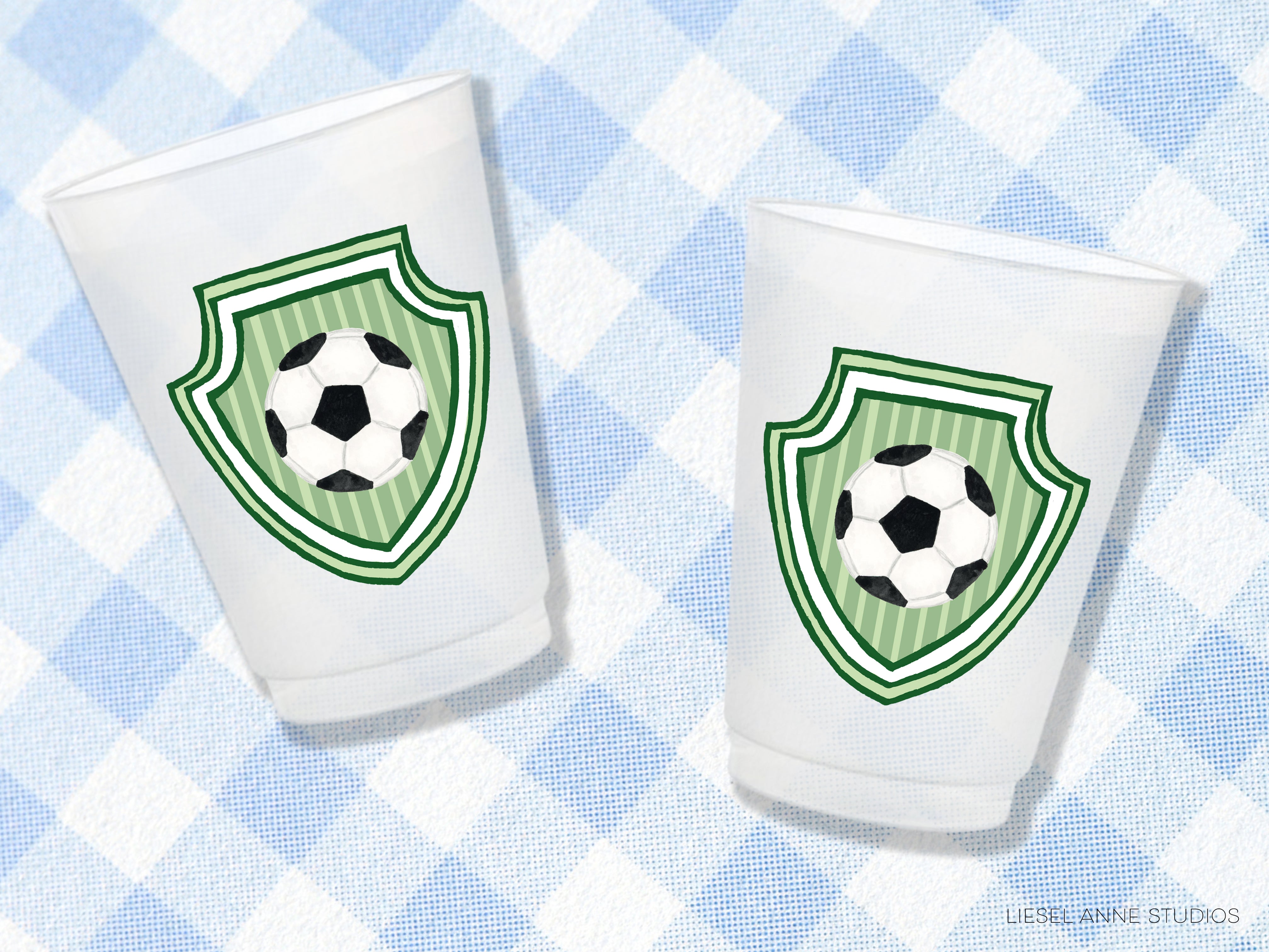 Two white plastic cups with green soccer ball designs on them, placed on a blue and white checkered background.