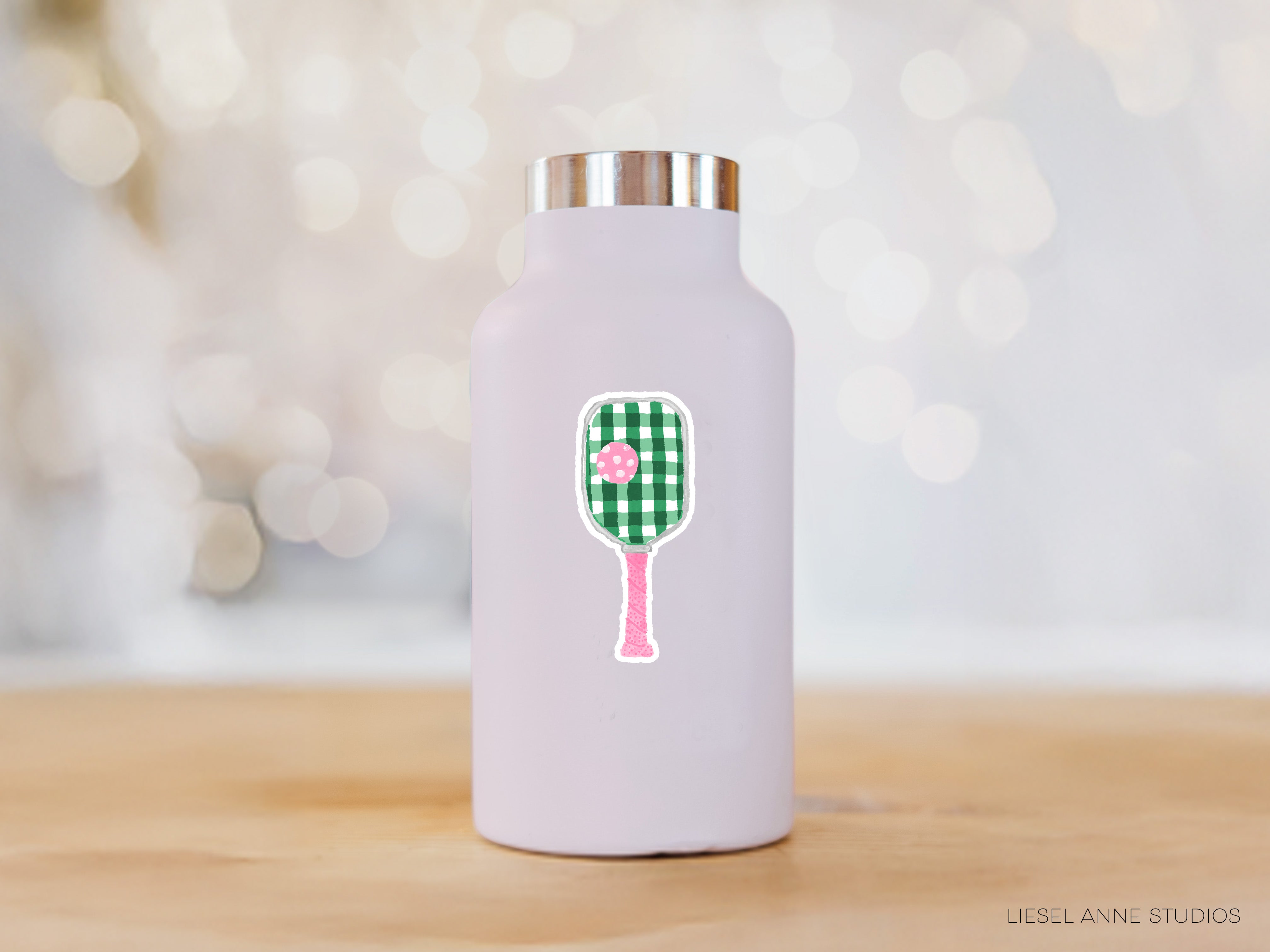 A white water bottle with a green and white tennis racket sticker on it, placed on a wooden surface against a blurred background.