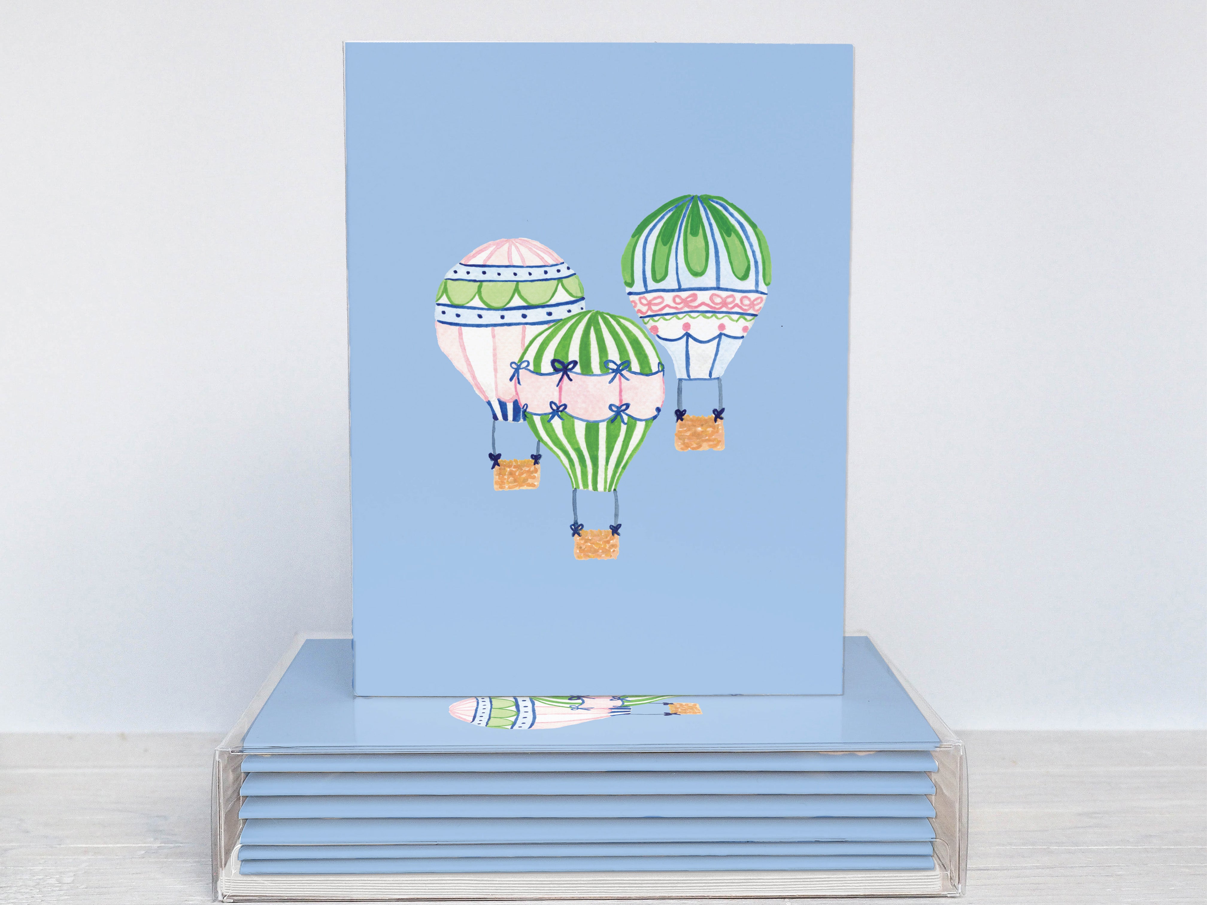 A blue card with a colorful illustration of three hot air balloons floating in the sky.