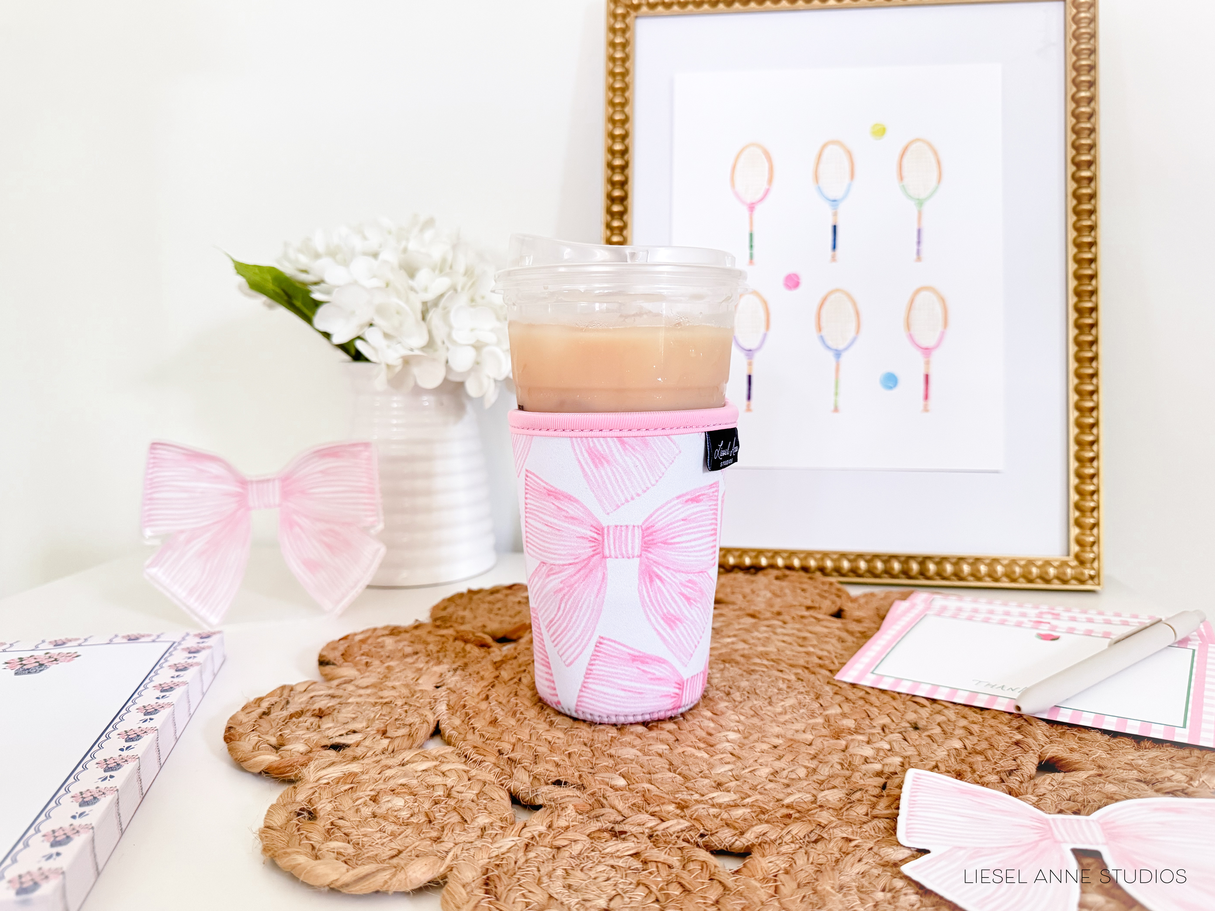 a table with a cup of coffee, a framed picture of tennis rackets, a vase of white flowers, and a decorative bow.