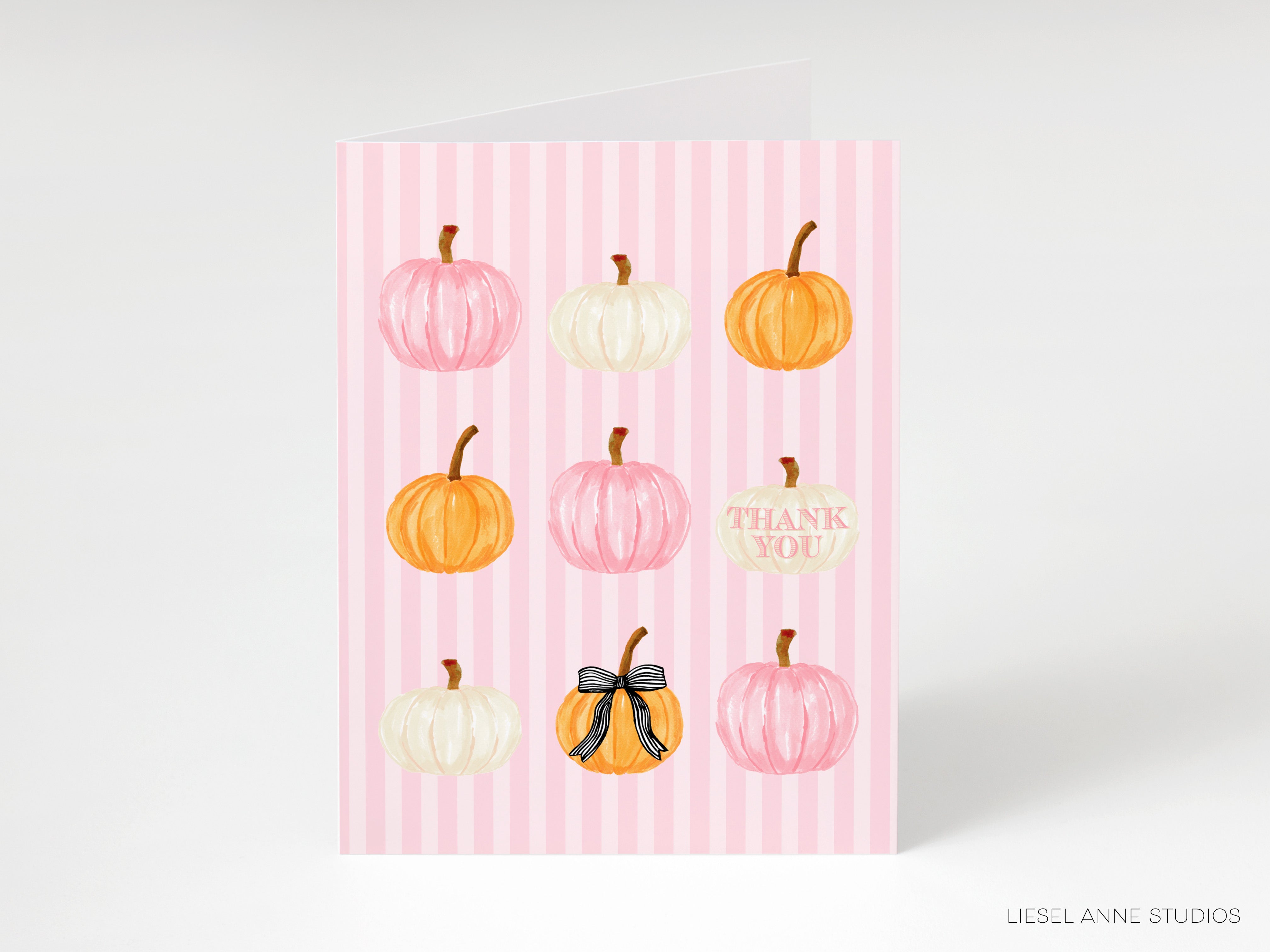 A pink striped card with nine pumpkins of various sizes and colors, including white, orange, and yellow, arranged in a 3x3 grid.