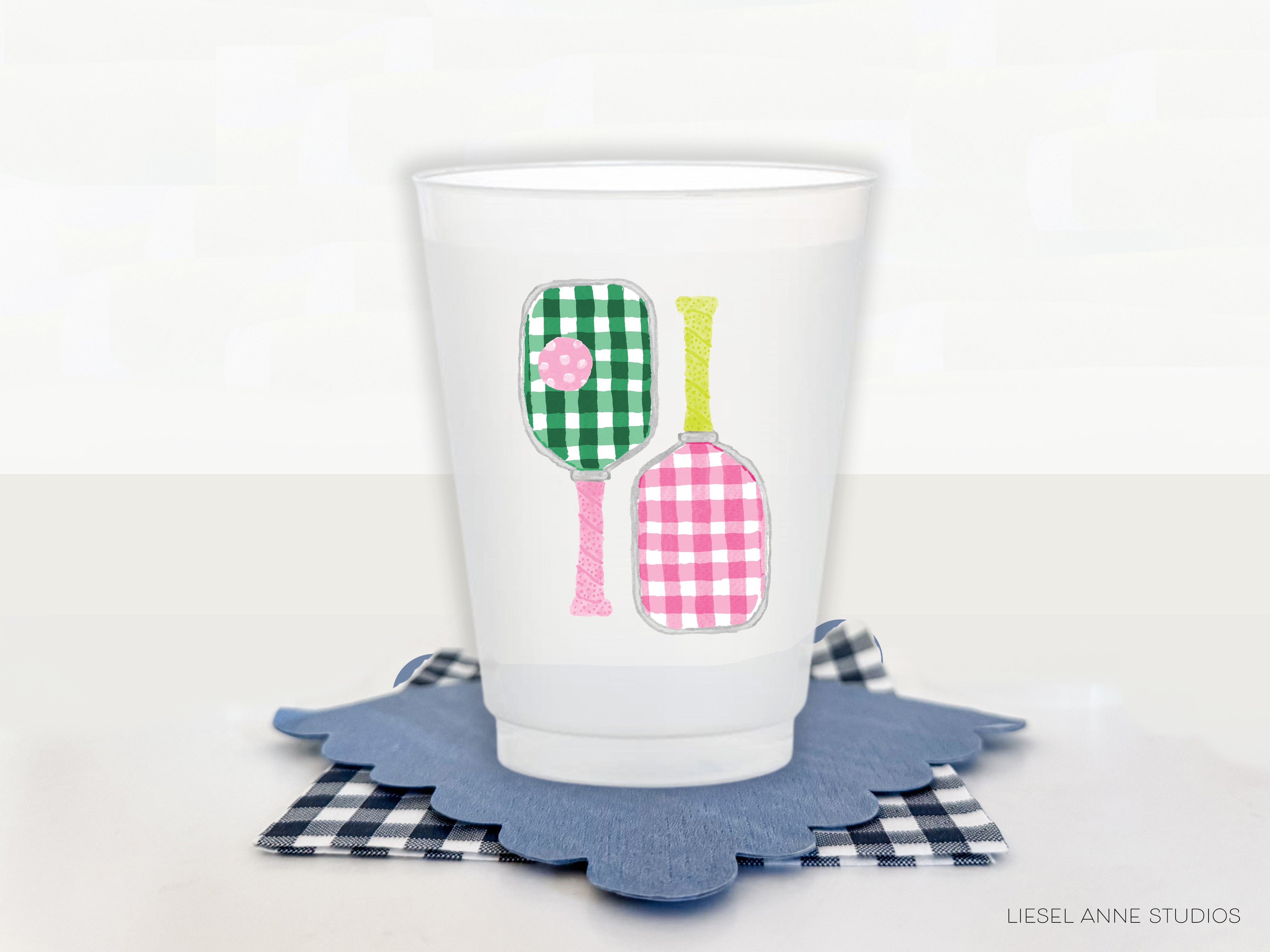 A white plastic cup with a colorful design of two tennis rackets on it, placed on a blue coaster.