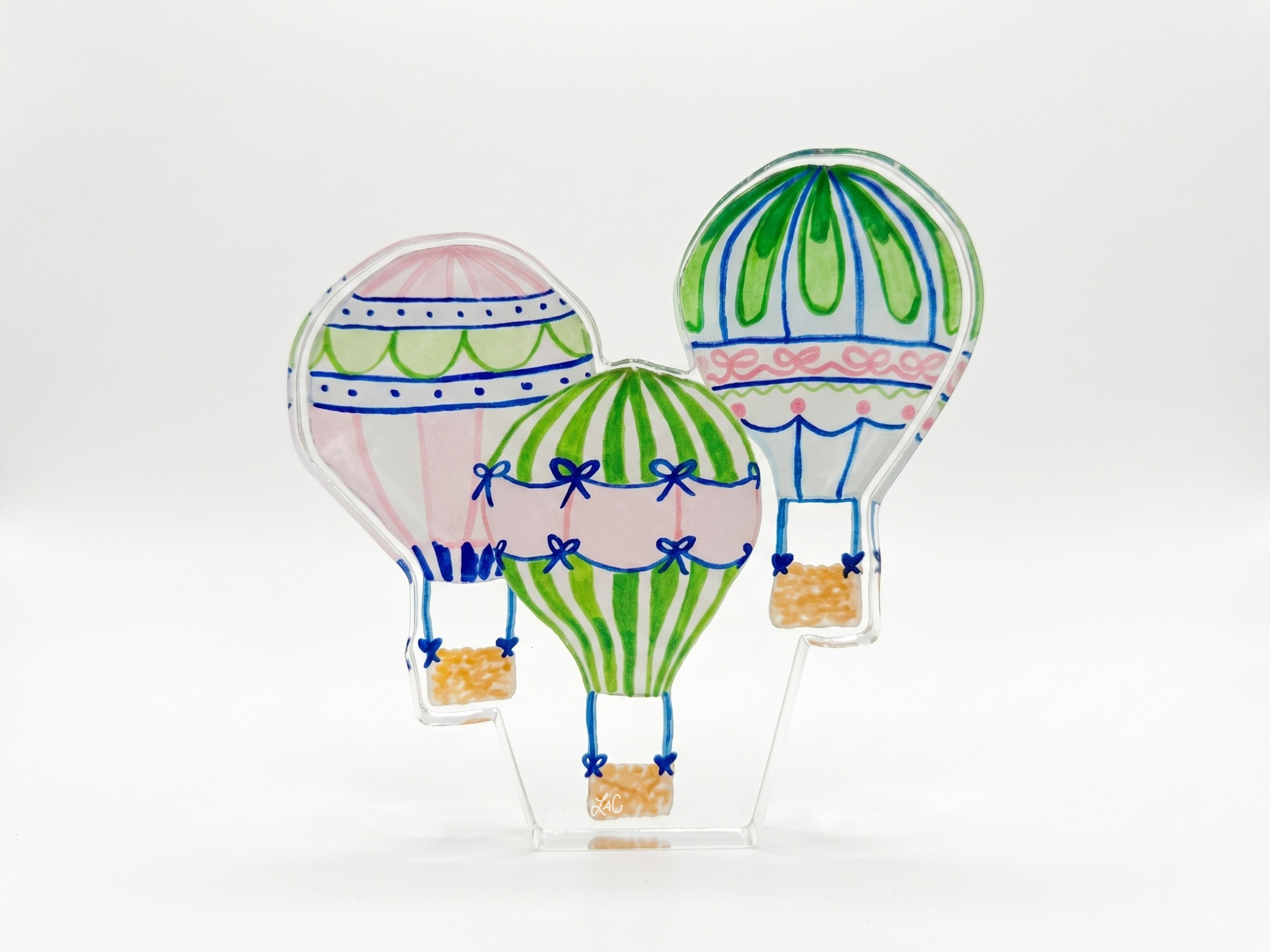 A trio of colorful hot air balloons in various designs, including a pink and white balloon, a green and white striped balloon, and a blue and white striped balloon, all floating against a plain white background.