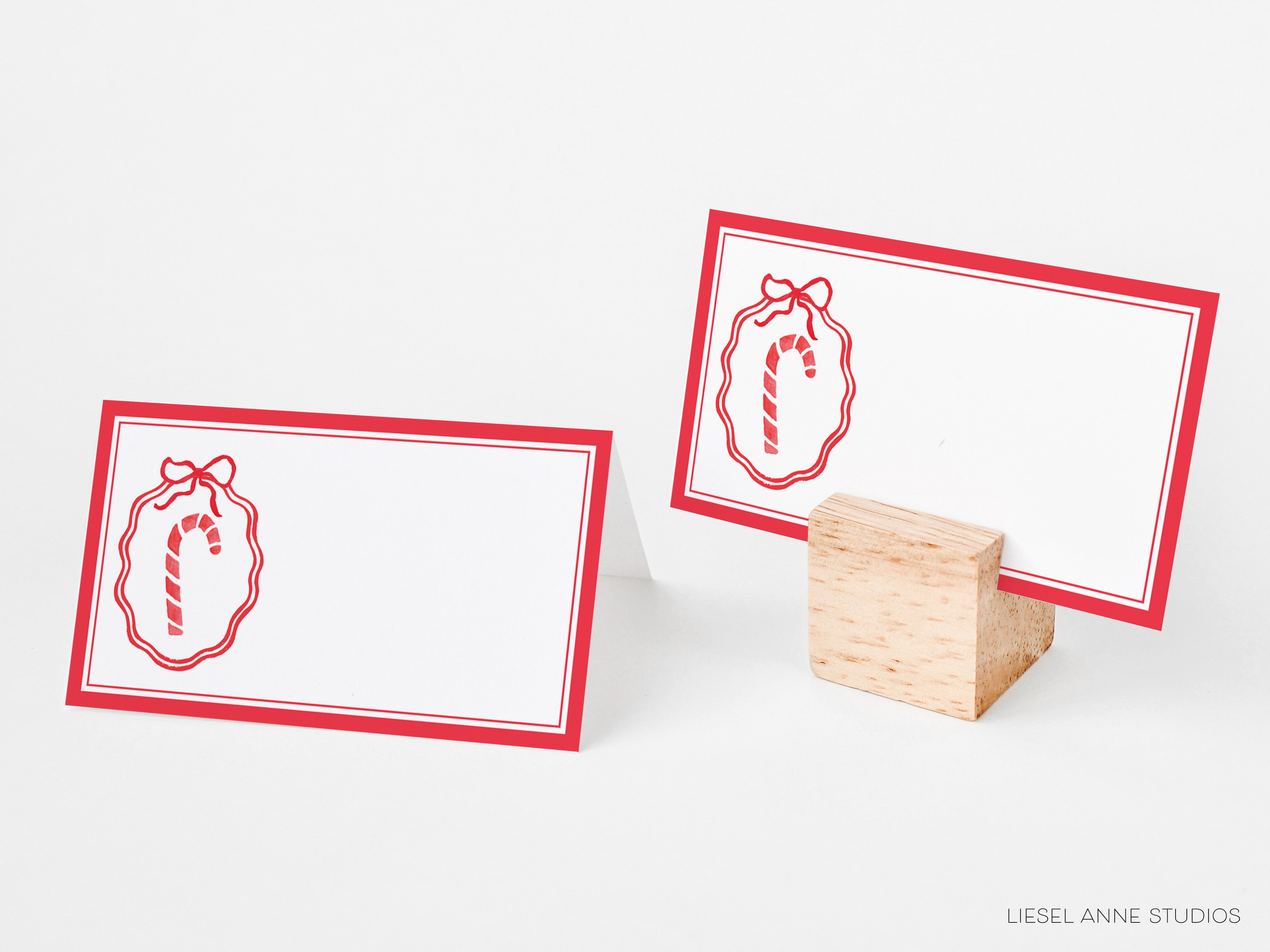 two red place cards with a candy cane design, placed on a wooden stand.