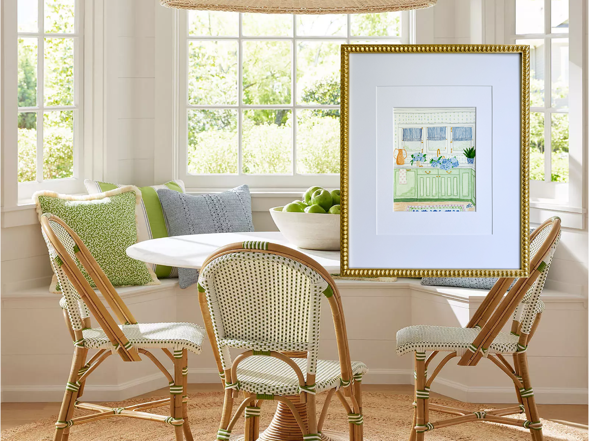 a cozy dining area with a white table and chairs, a framed picture of a kitchen scene, and a window overlooking a garden.