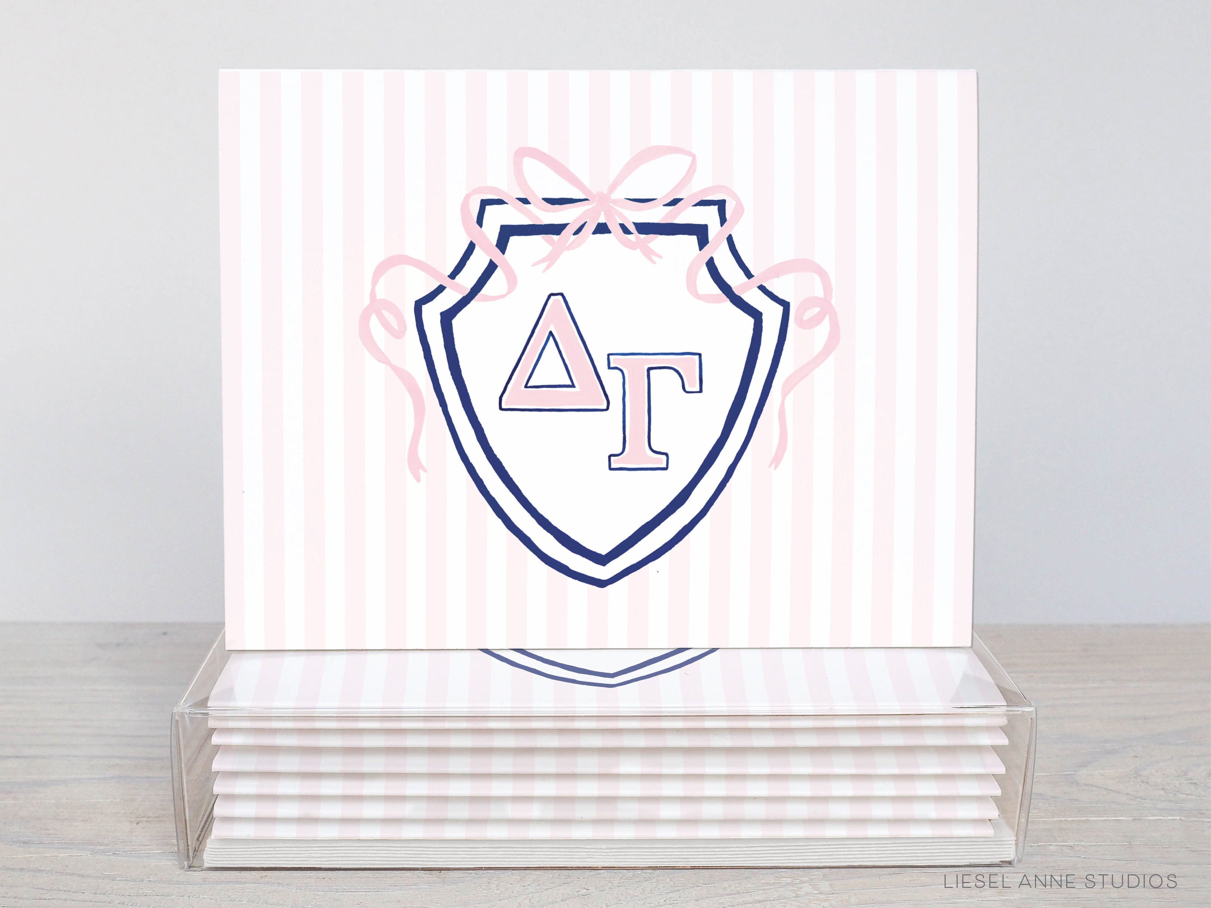 A stack of pink and white striped greeting cards with a blue and white shield-shaped design featuring the letters "ΔΩ" and a bow.