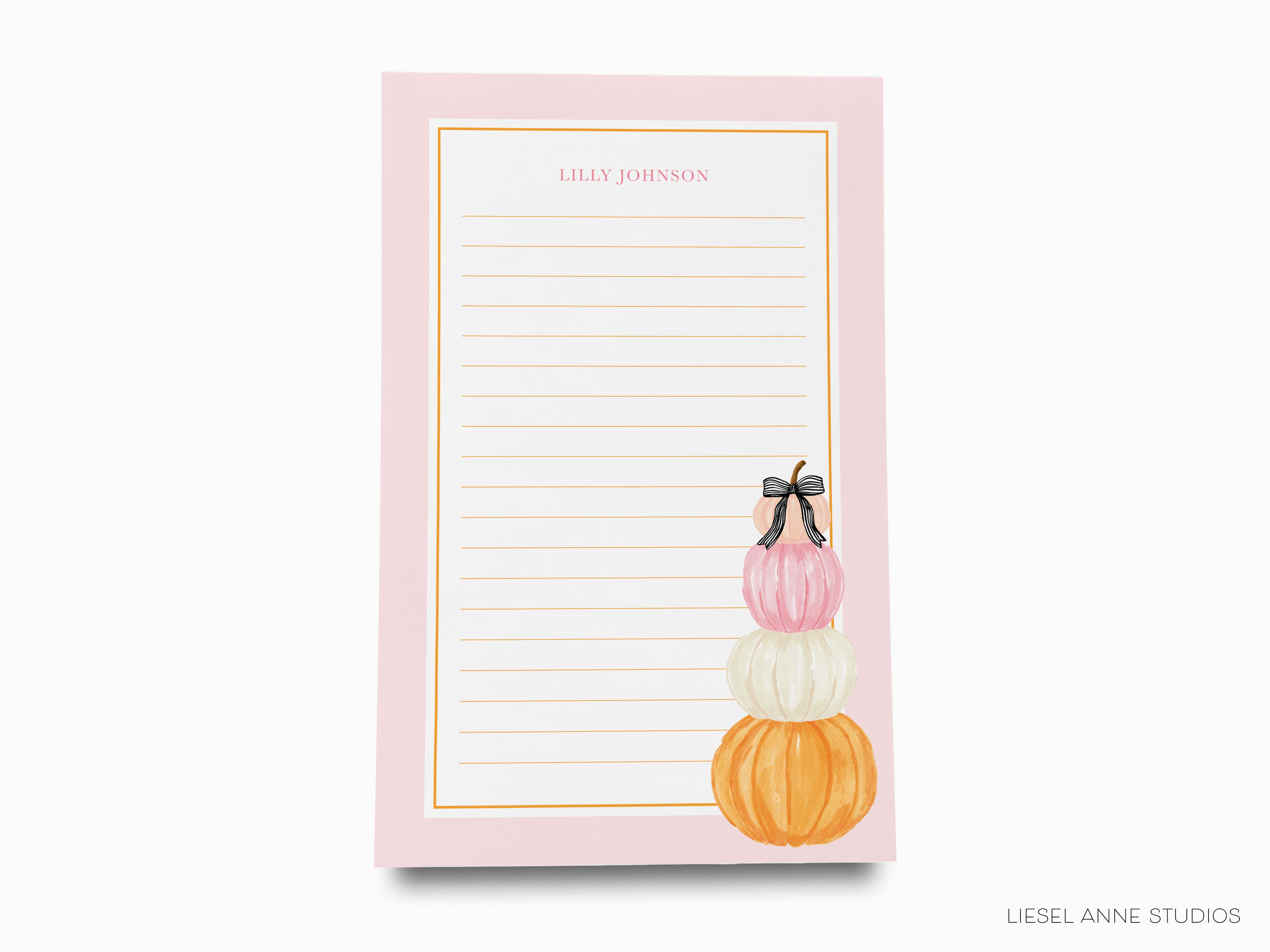 A pink notepad with a blank lined page and a decorative illustration of three stacked pumpkins with bows on the side.
