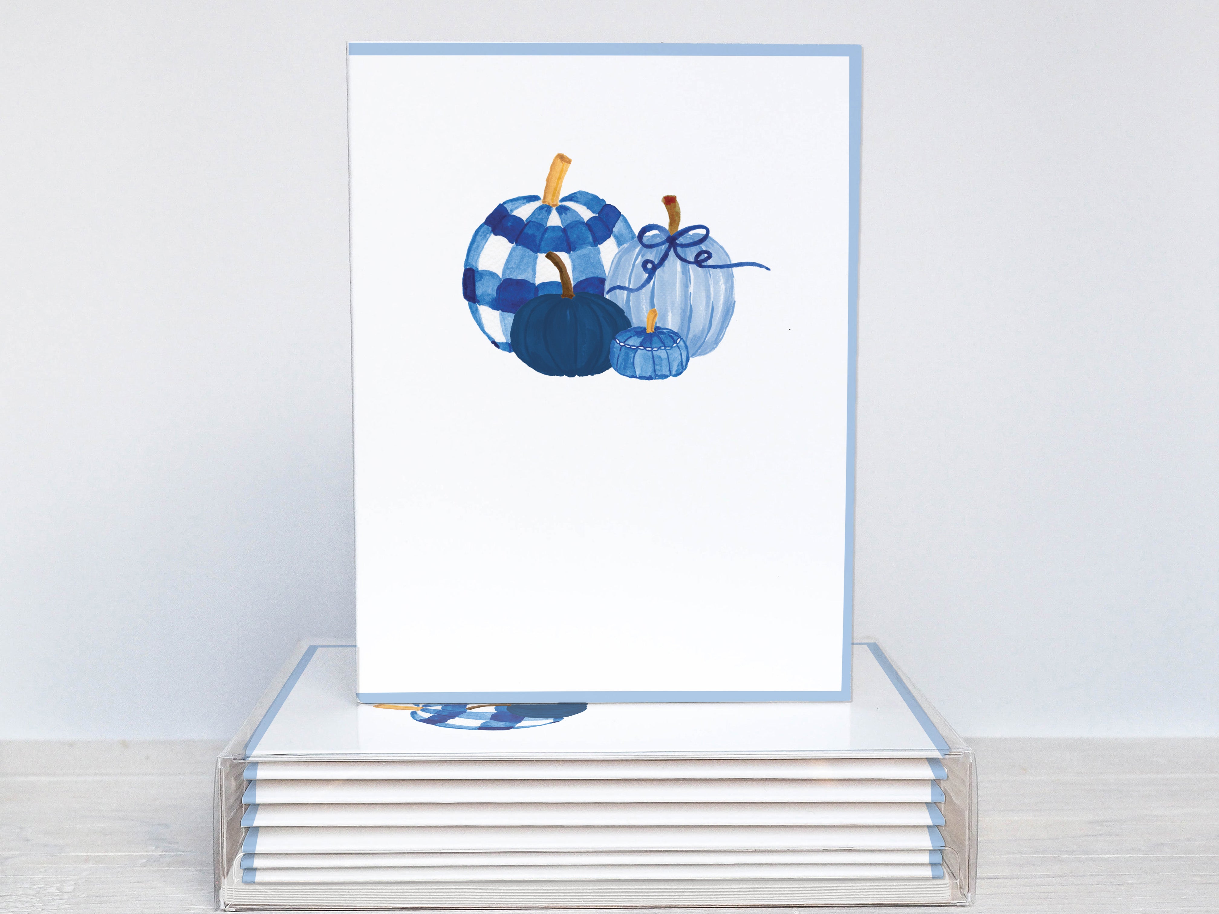 A white card with a blue and white illustration of pumpkins on it, placed on top of a stack of similar cards.