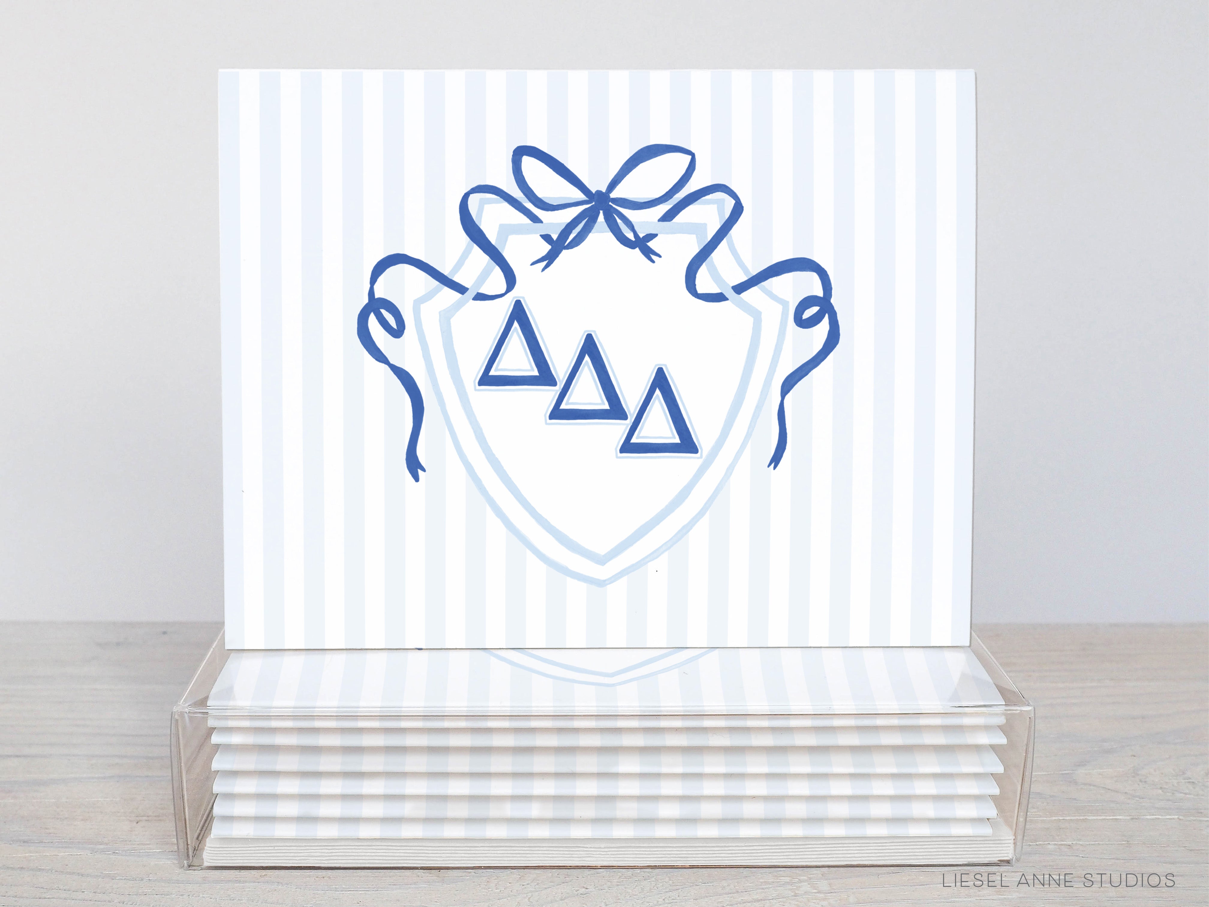 A stack of white greeting cards with a blue and white striped design featuring a shield-shaped emblem with three blue triangles and a blue ribbon.