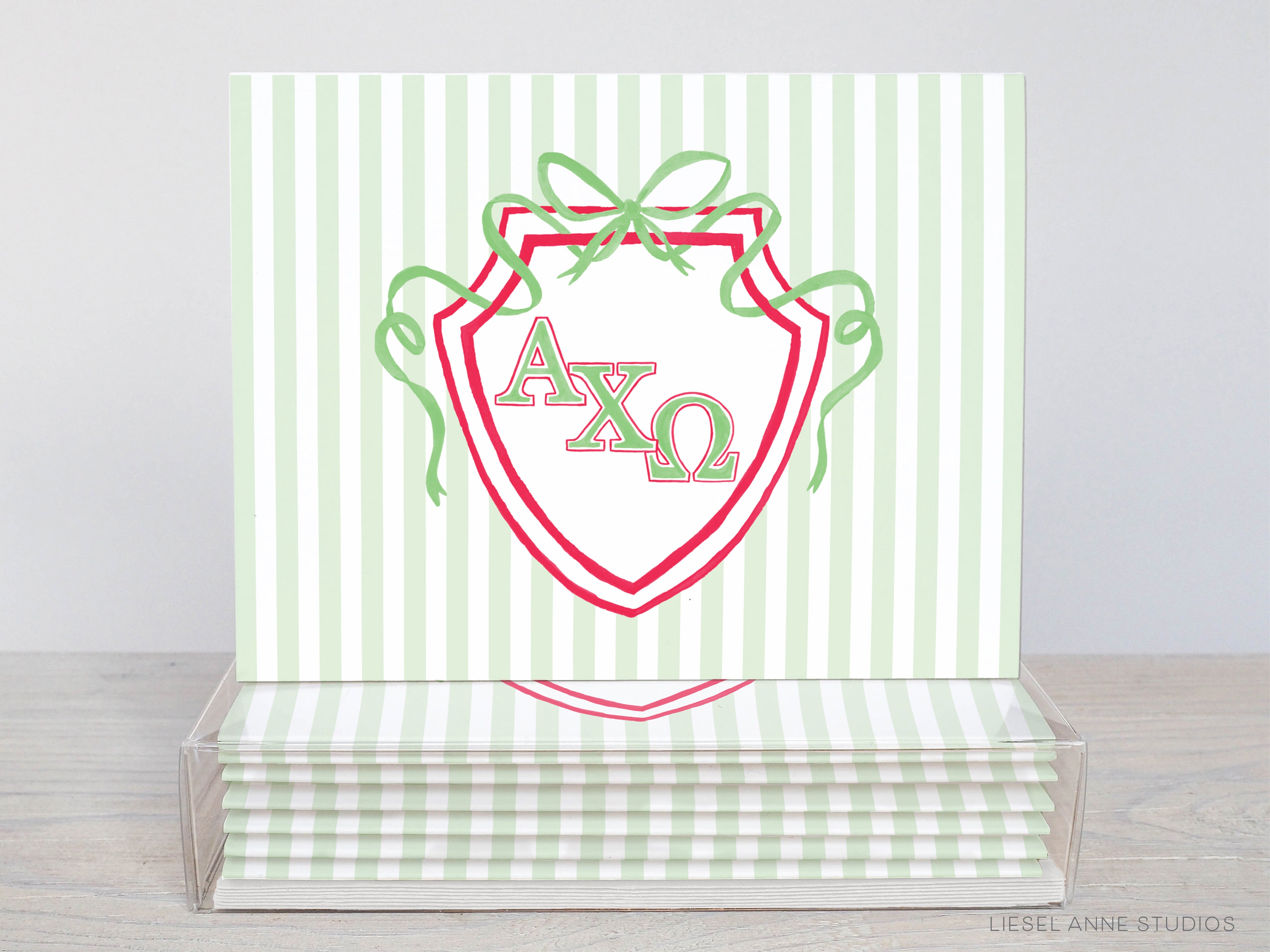 A stack of green and white striped greeting cards with a shield-shaped design featuring the letters 'AXO' and a bow.