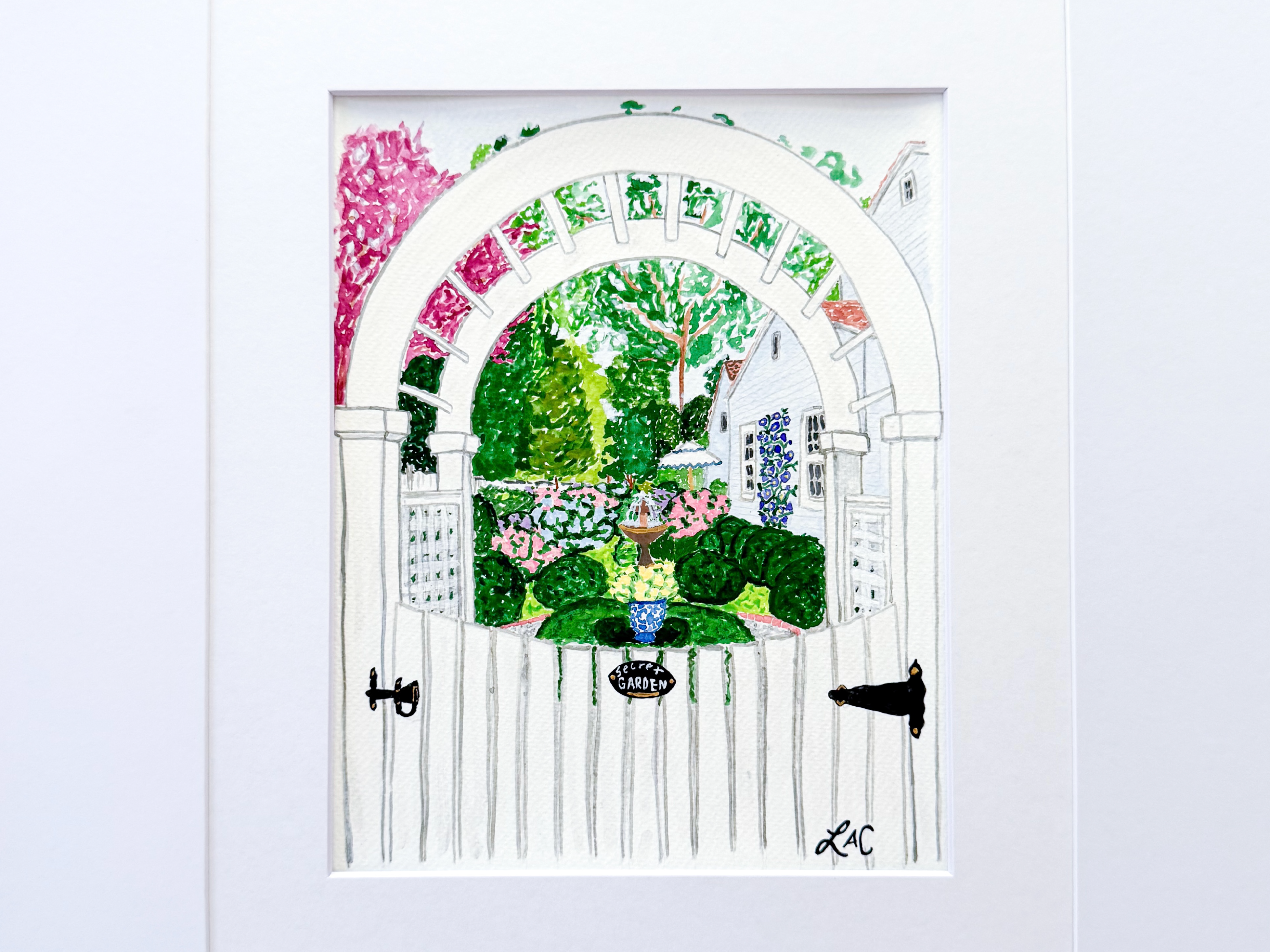 A white wooden gate with a decorative archway, surrounded by a lush garden with colorful flowers and greenery.