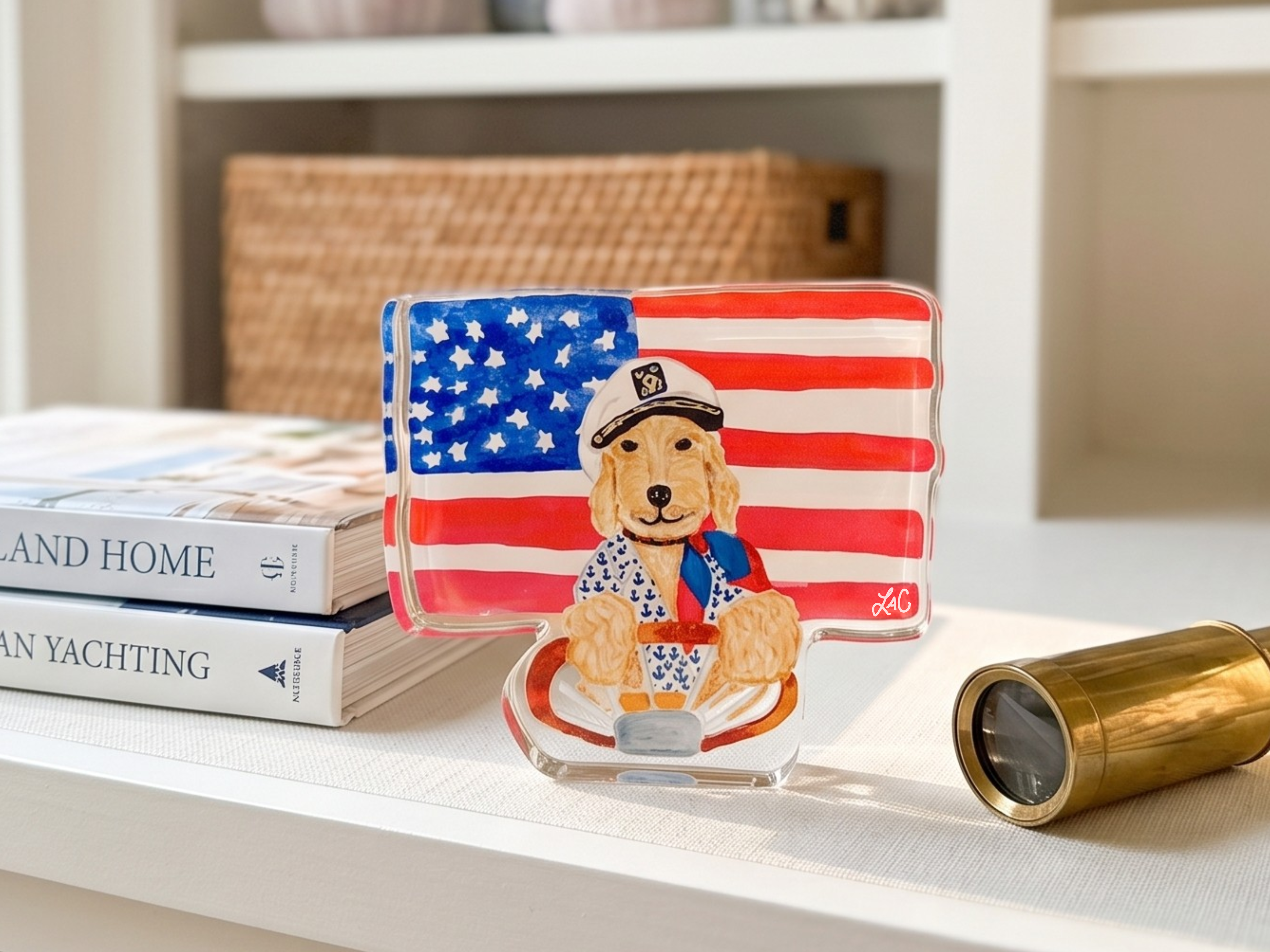 a clear glass sculpture of a dog wearing a hat and holding an American flag, placed on a white surface next to a pair of binoculars and a book titled "LAND AND HOME YACHTING".