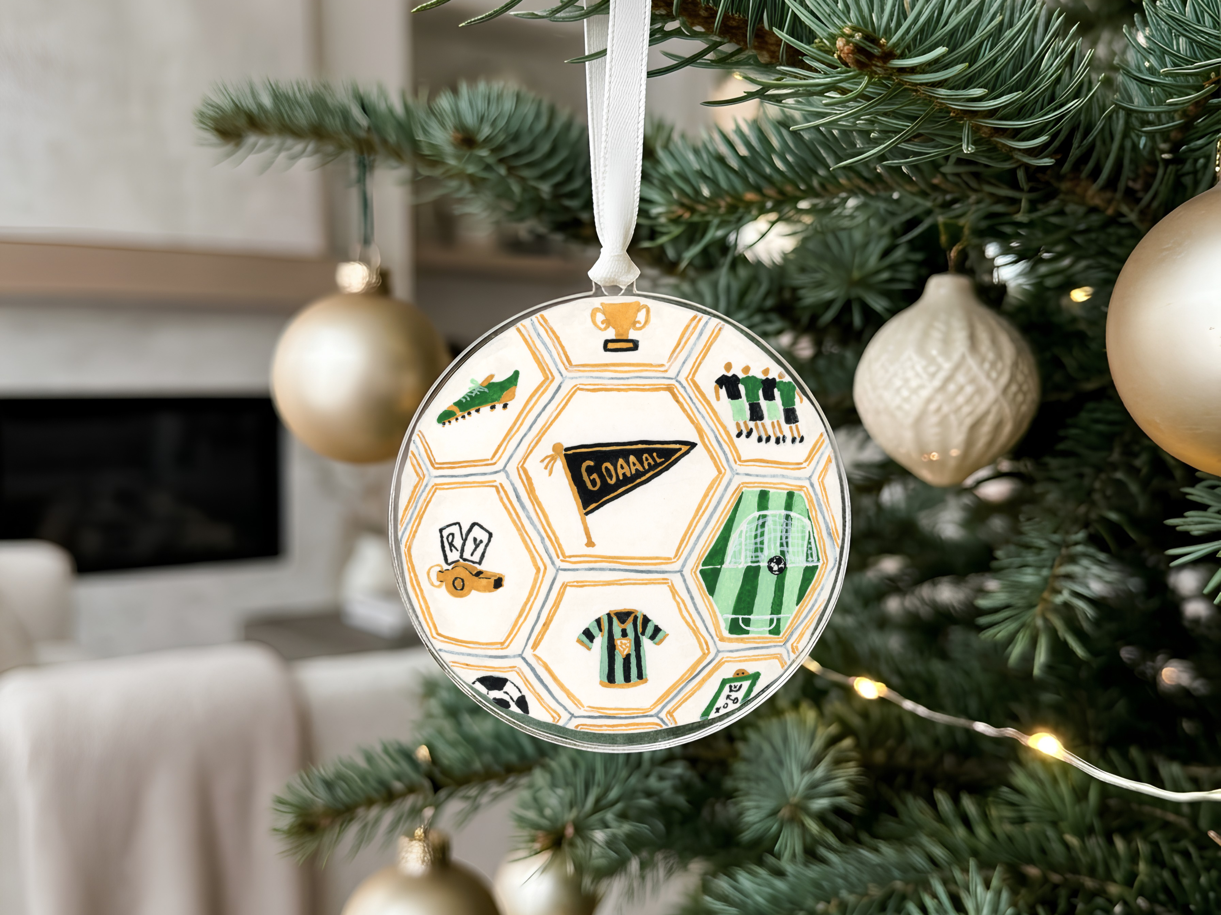A round ornament hanging from a Christmas tree, featuring soccer-related designs and a flag.