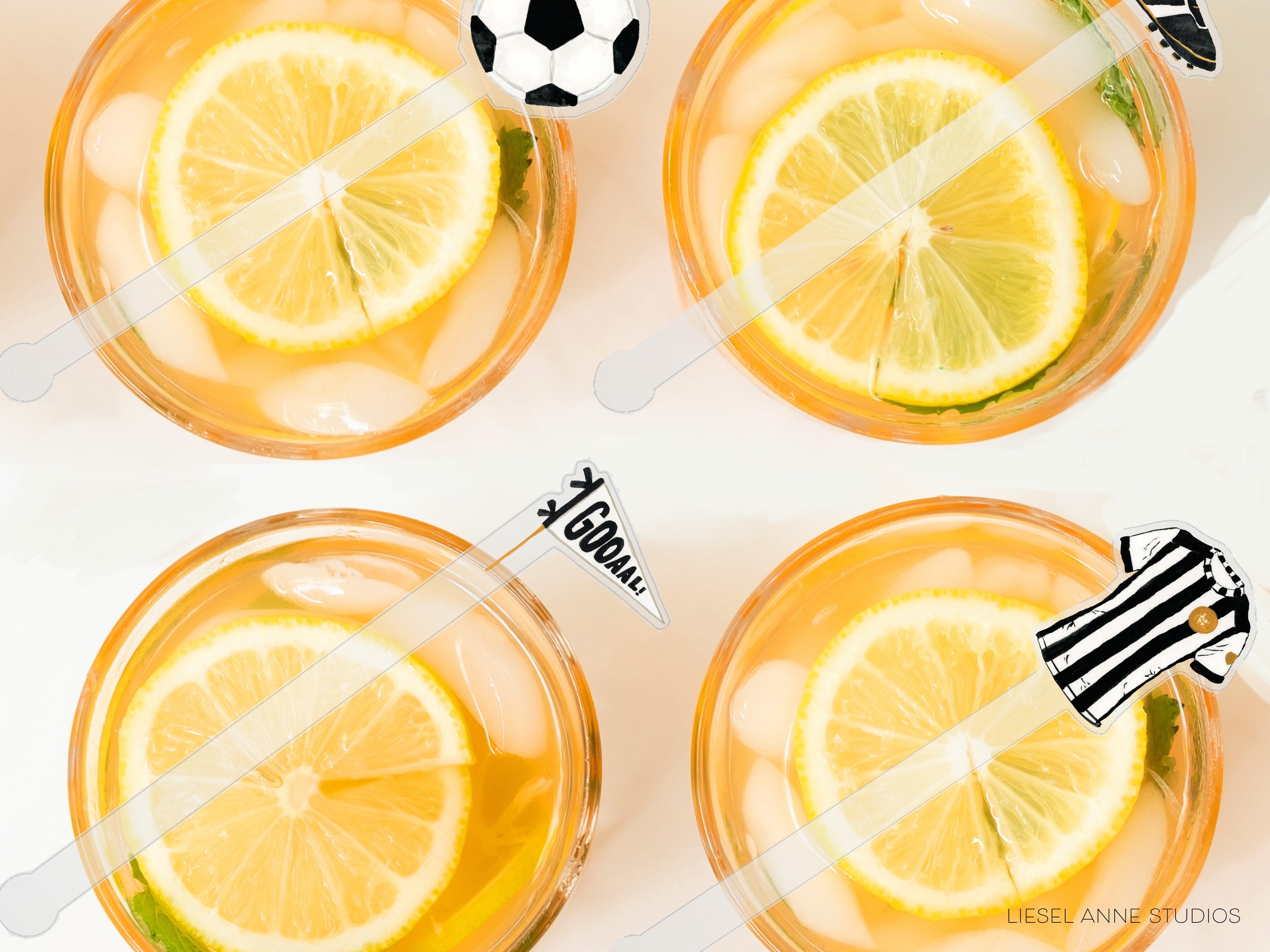 four glasses filled with a yellow liquid, each containing a slice of lemon. The glasses are placed on a white surface, and there are lemon slices and a soccer ball decoration on the glasses.