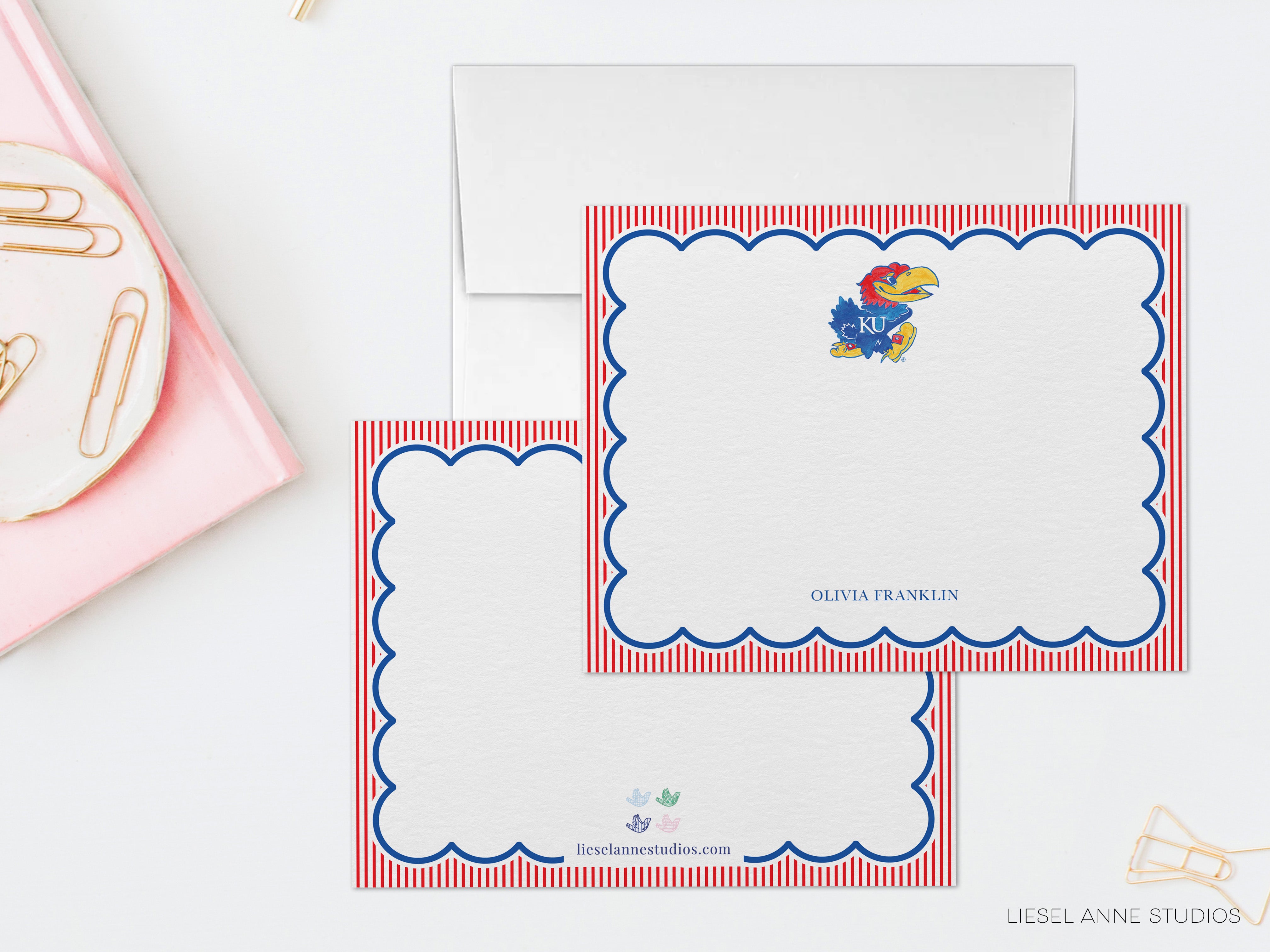 two blank greeting cards with a red and white striped border and a Kansas City University (KC) logo. The cards are placed on a white surface, with a pink object and some gold clips nearby.