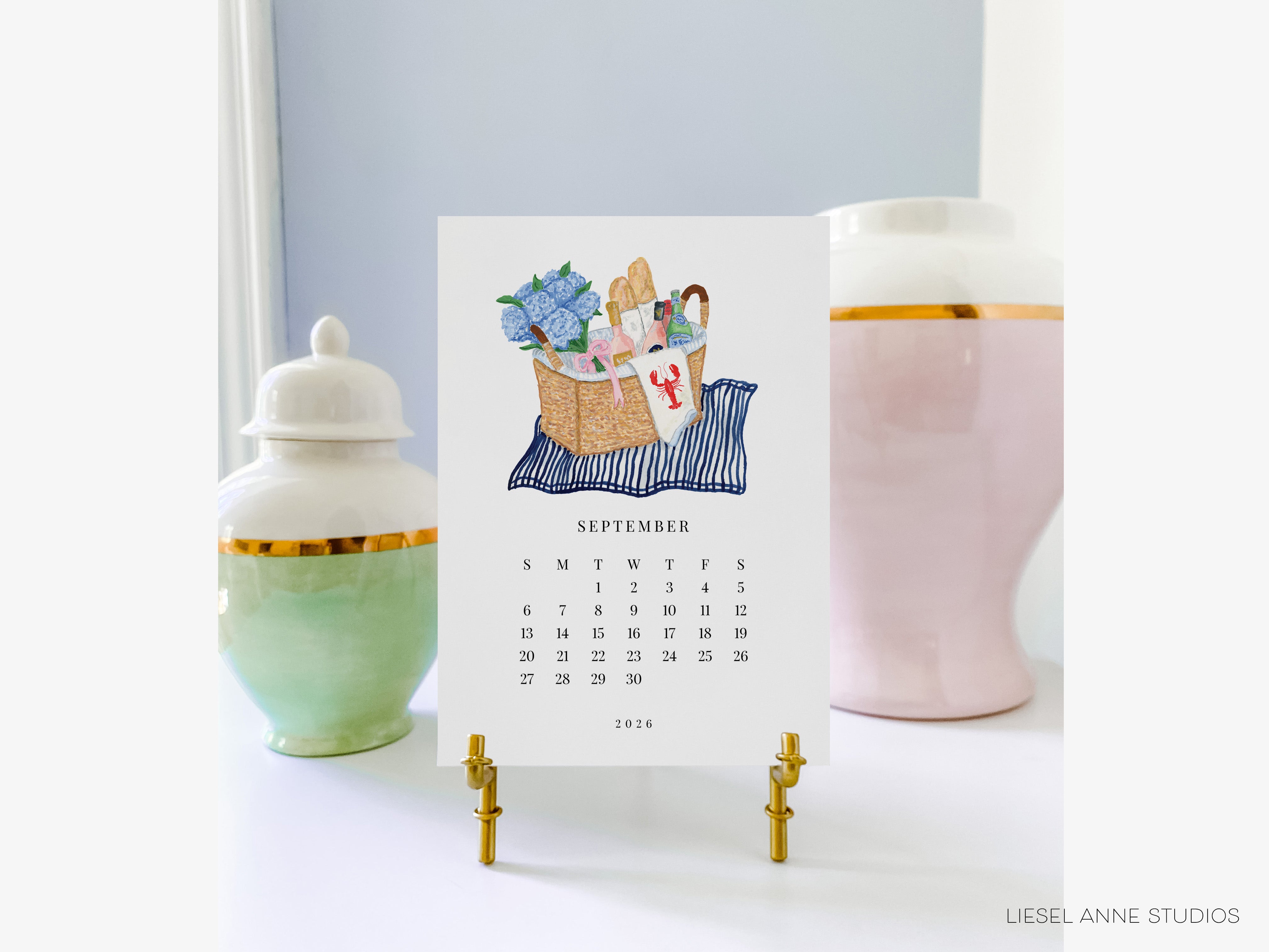 A September 2016 calendar with a blue and white striped background and a basket of blue flowers, placed on a white surface between two ceramic vases.