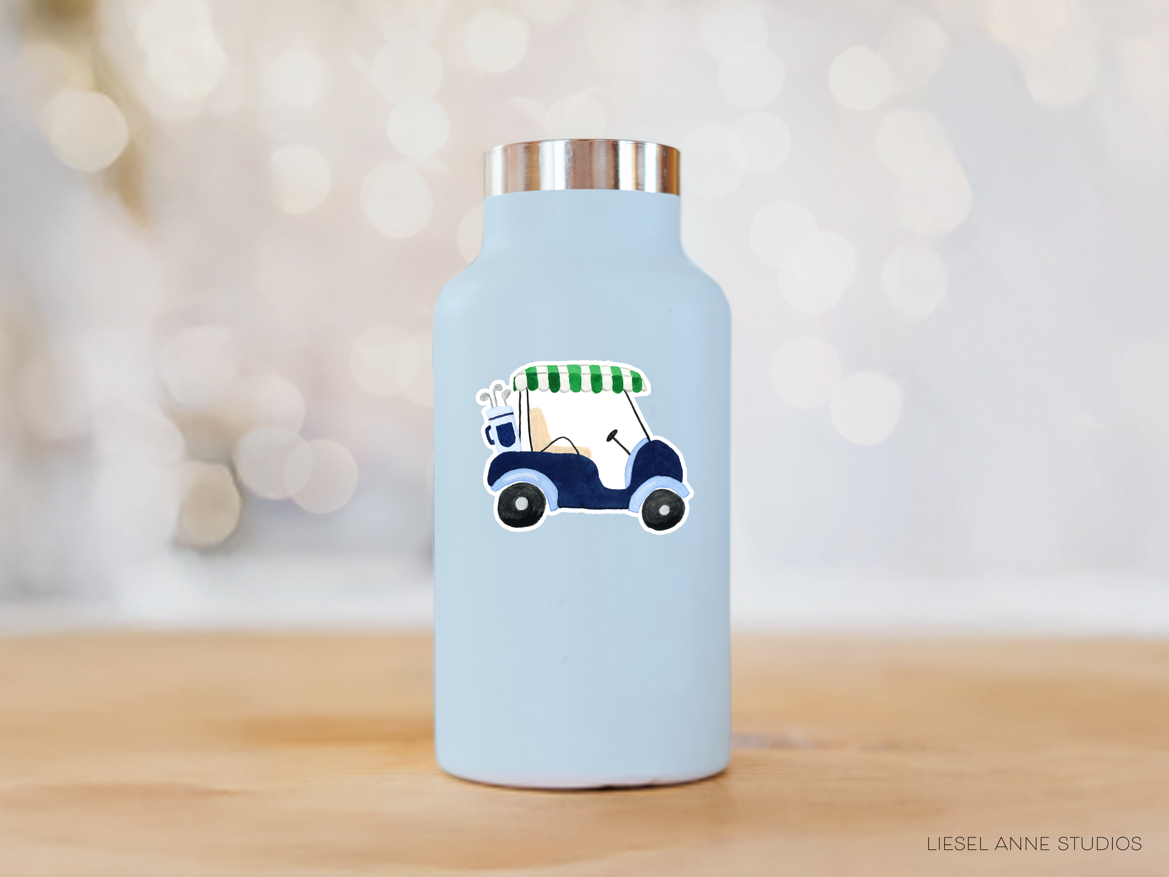 A light blue water bottle with a golf cart sticker on it, placed on a wooden surface against a blurred background.