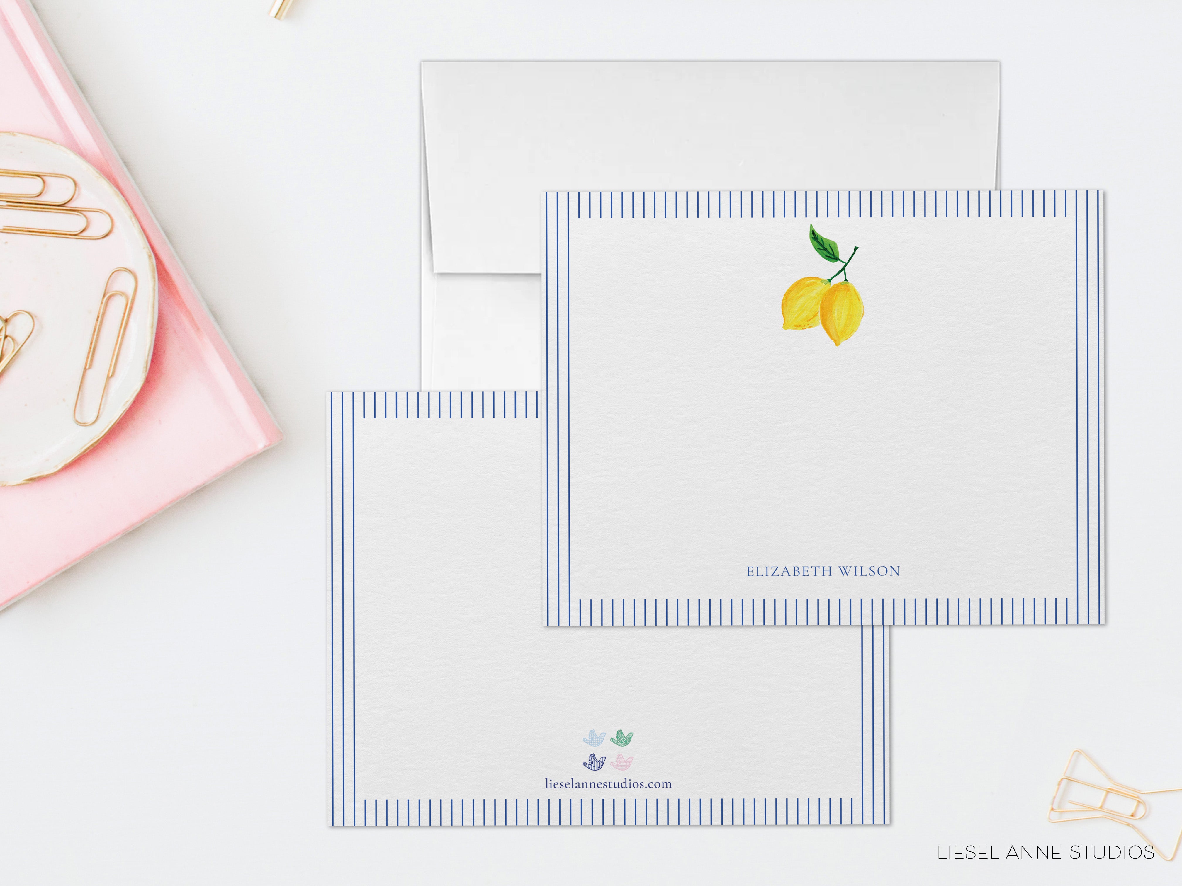 two blank stationery cards with a lemon design, placed on a white surface alongside a pink object and some office supplies.