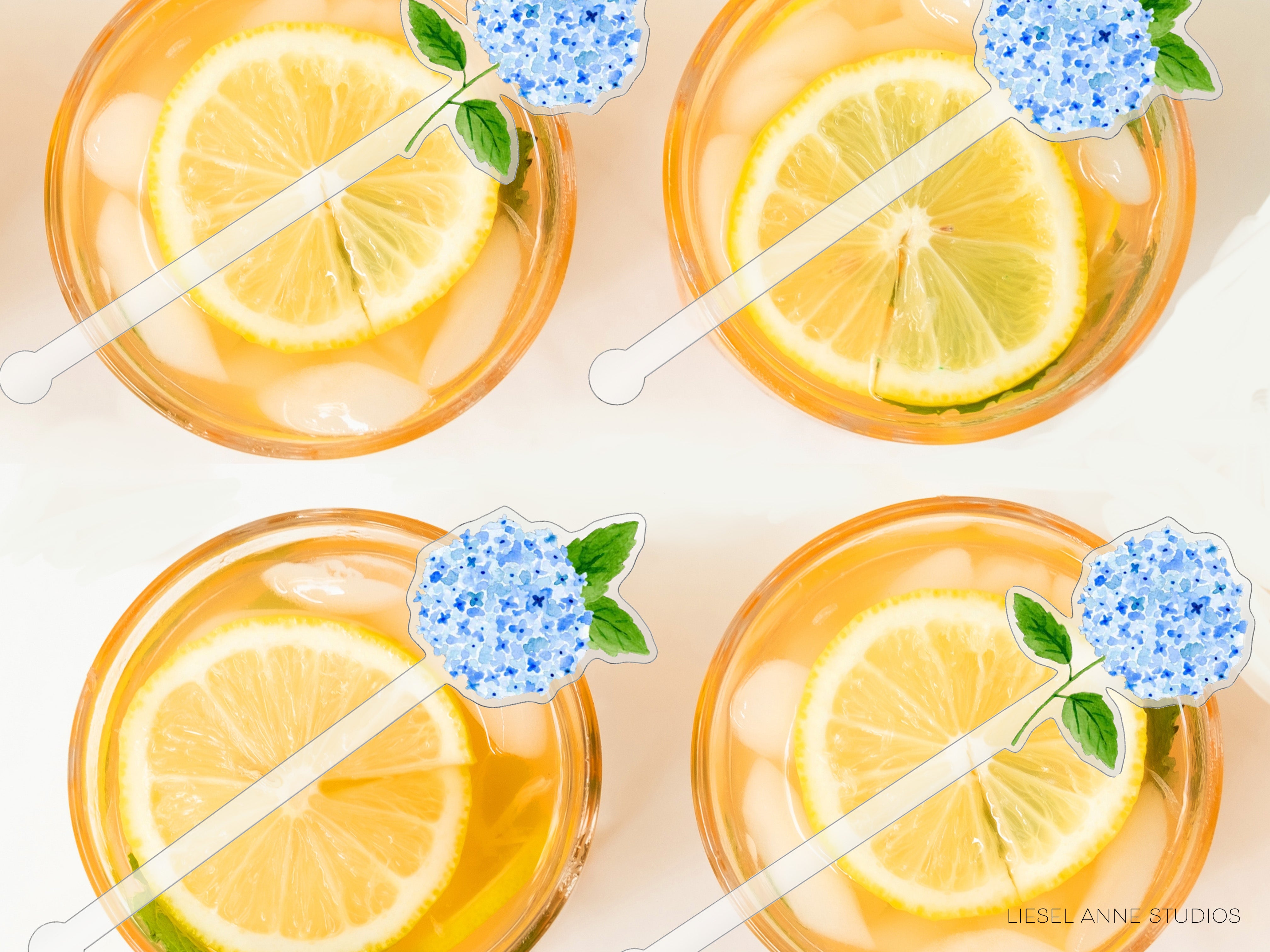 four glasses filled with a yellow liquid, each containing a slice of lemon and a blue flower decoration.