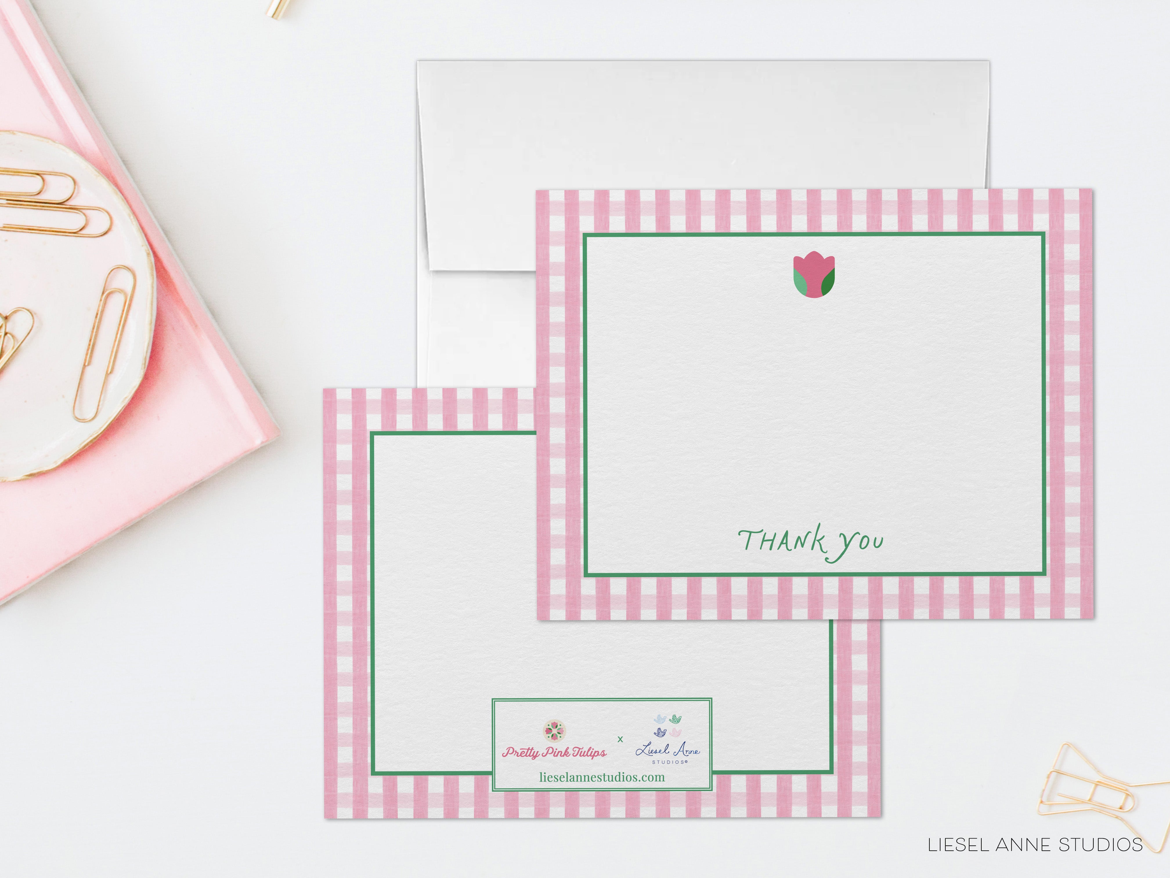 two pink and white checkered cards with a blank space for writing a "Thank you" message. The cards are placed on a white surface, with a pink plate and some gold clips nearby.