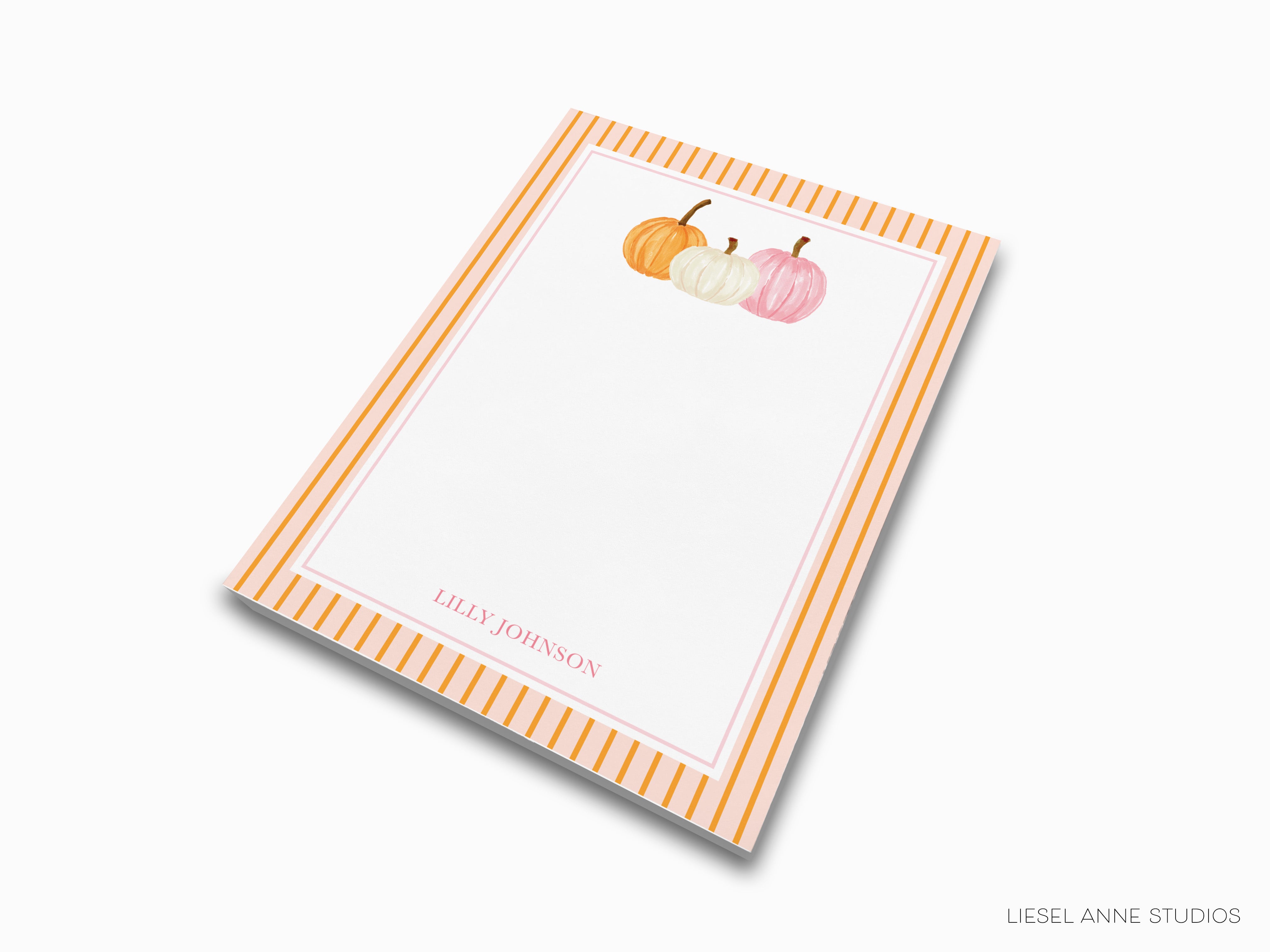 A white notepad with a striped border and a design of three pumpkins in different colors - orange, white, and pink.