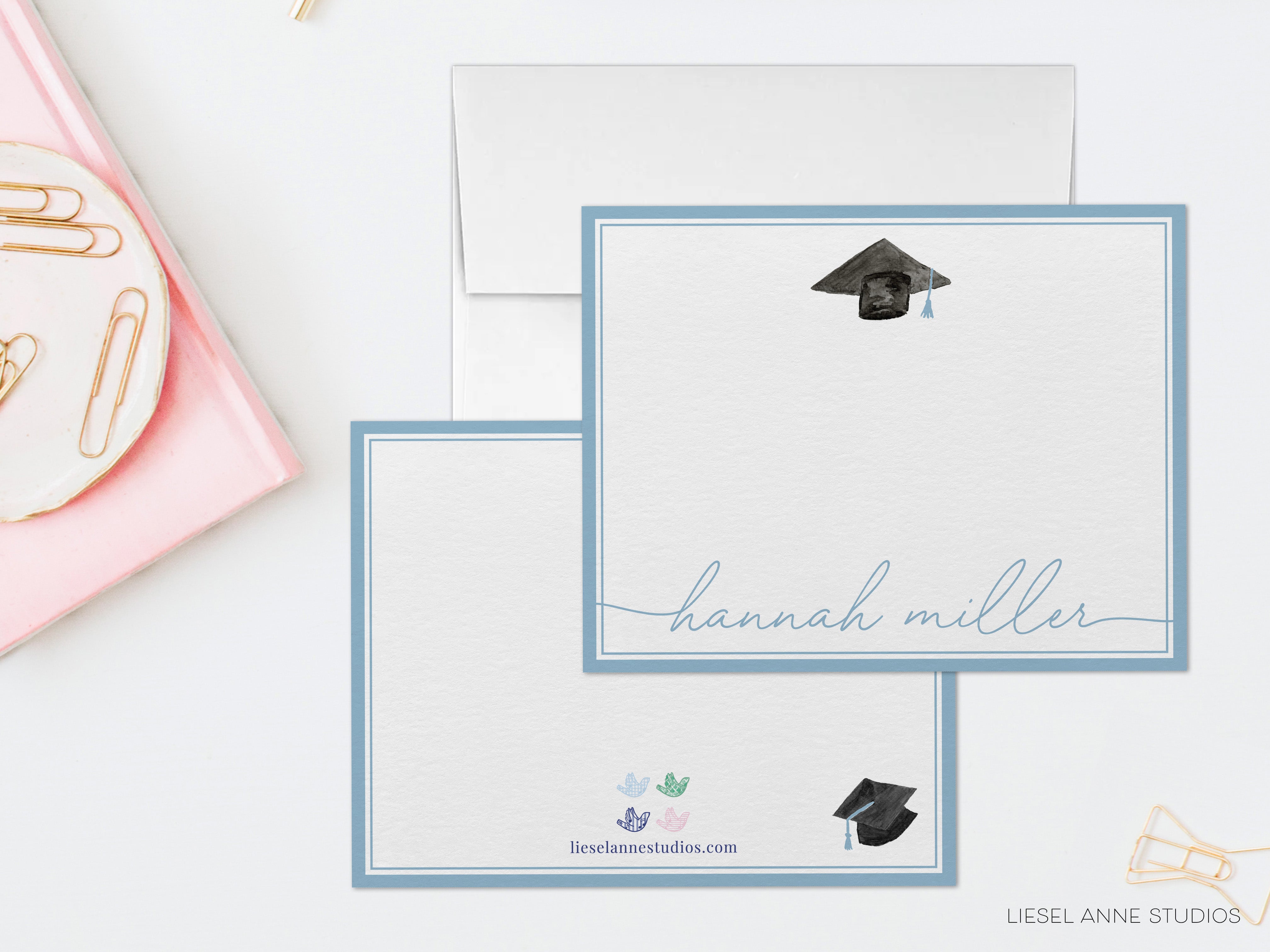 a set of personalized graduation cards with the name 'Hannah Miller' written on them. The cards are placed on a white surface, with a pink object and some office supplies visible in the background.