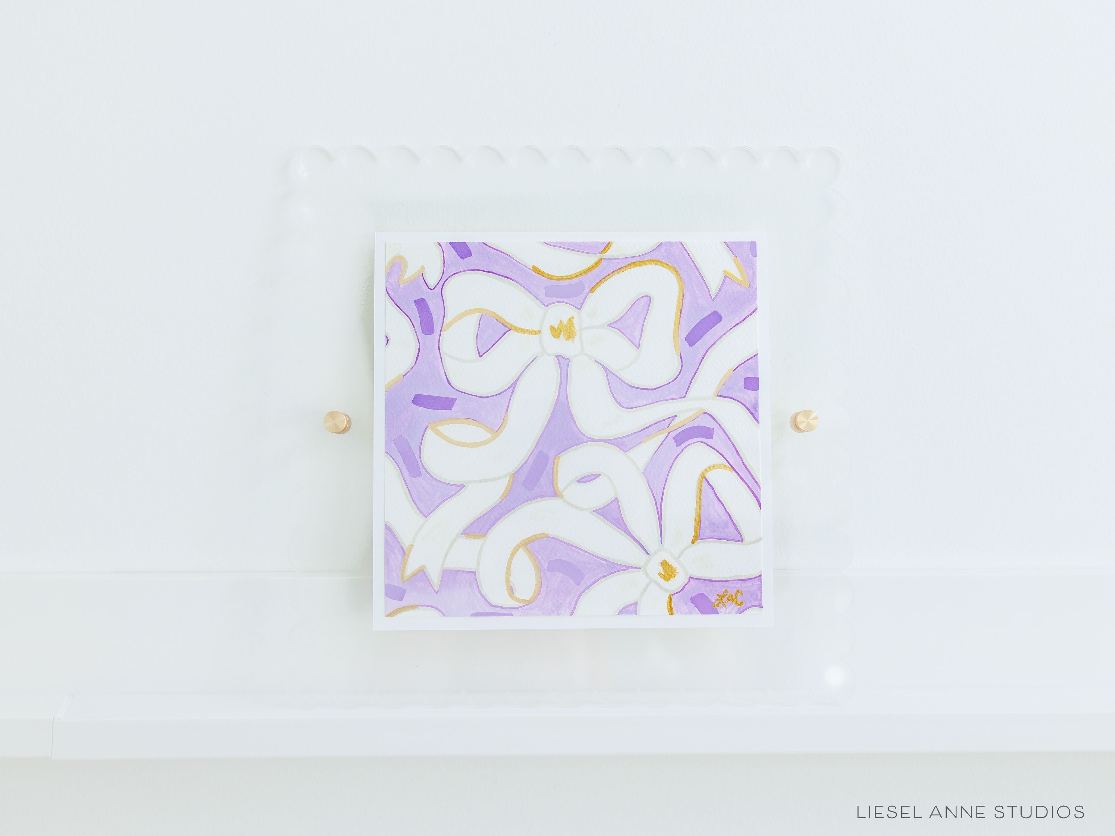 Golden Bows Lavender & White 04 [Original Artwork + Clear Scalloped Frame]-Original artwork measures 8"x8" | Hand-Painted with gouache on cold press watercolor paper | Matted and framed in an acrylic scalloped frame sized 12"x12" | Hanging hardware and acrylic clear stand included | Features our signature Golden Bows design with a lavender base, white bows and shimmery gold accents | Initialed in gold by Liesel Anne (the artist) on the front and signed and dated on the back-The Singing Little Bird